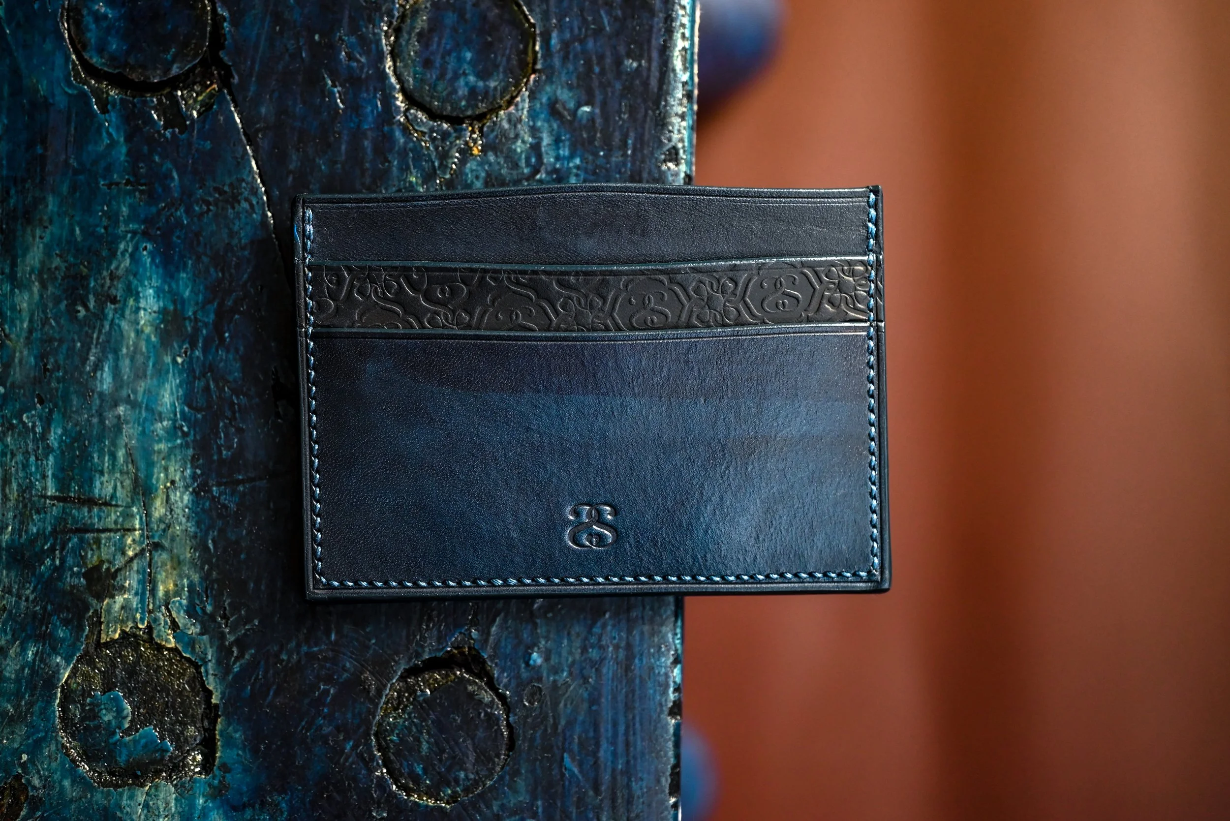 Un porte-carte en cuir tanné végétal et teint à l'indigo posé sur du bois teint à l'indigo