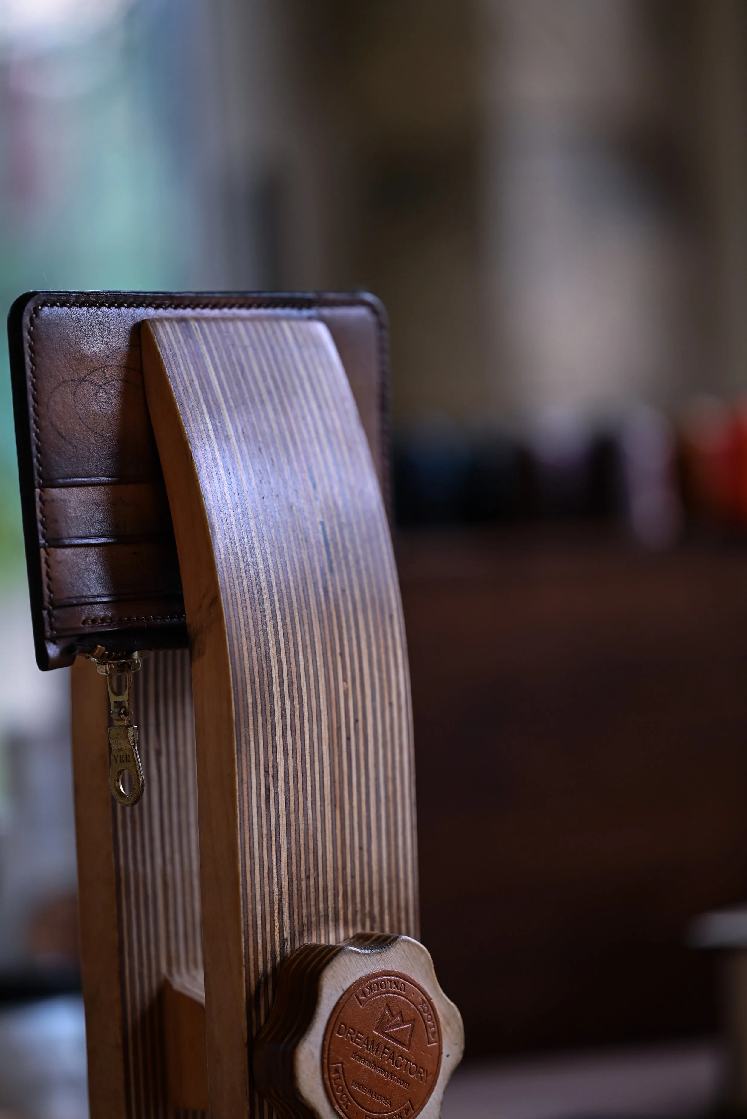 Un porte-feuille en cuir tanné végétal patiné en accroché dans un valet de couture en bois