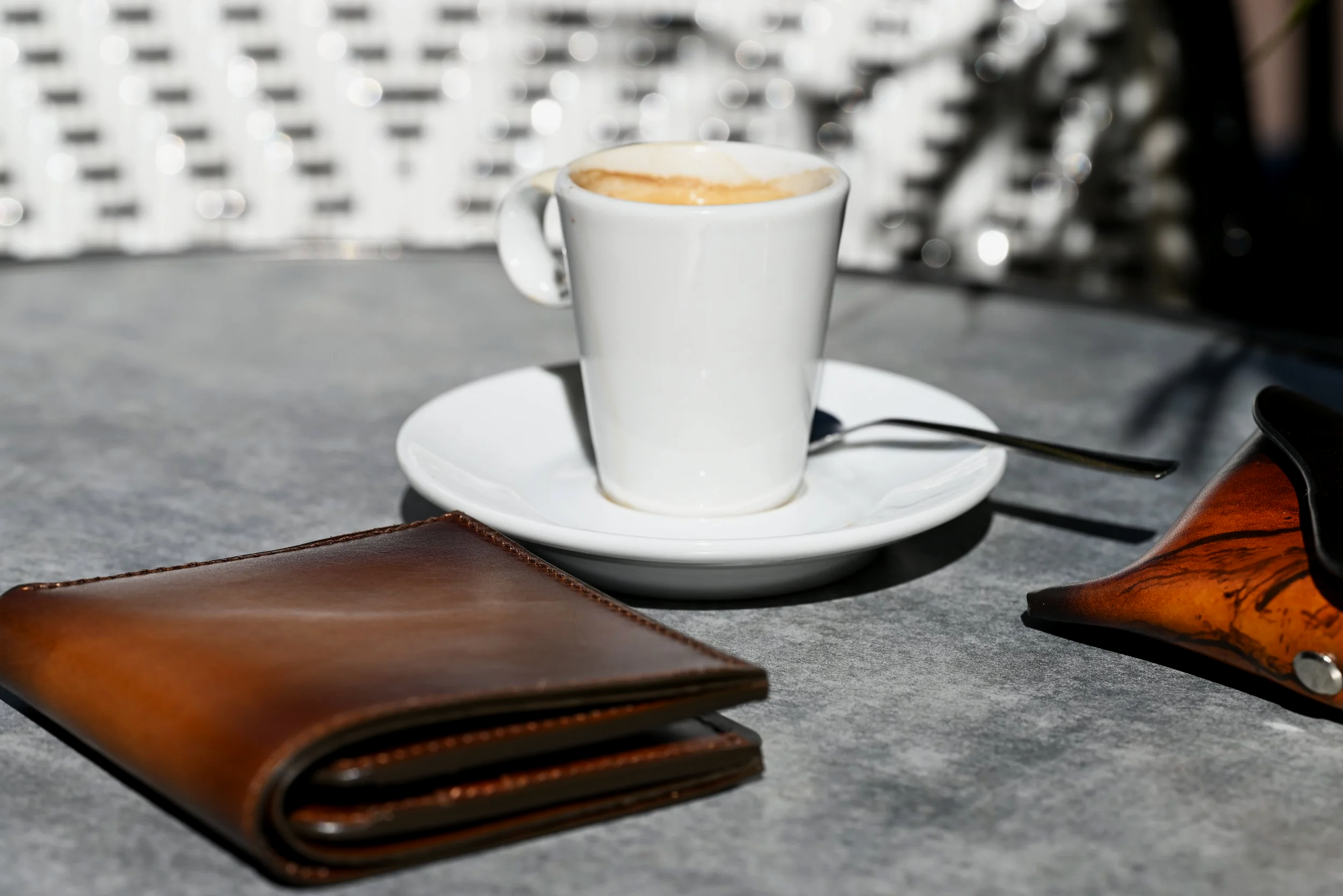 Un portefeuille et un bout d'étui à lunette en cuir végétal patinés à la main sont posé sur une table avec une tasse de café