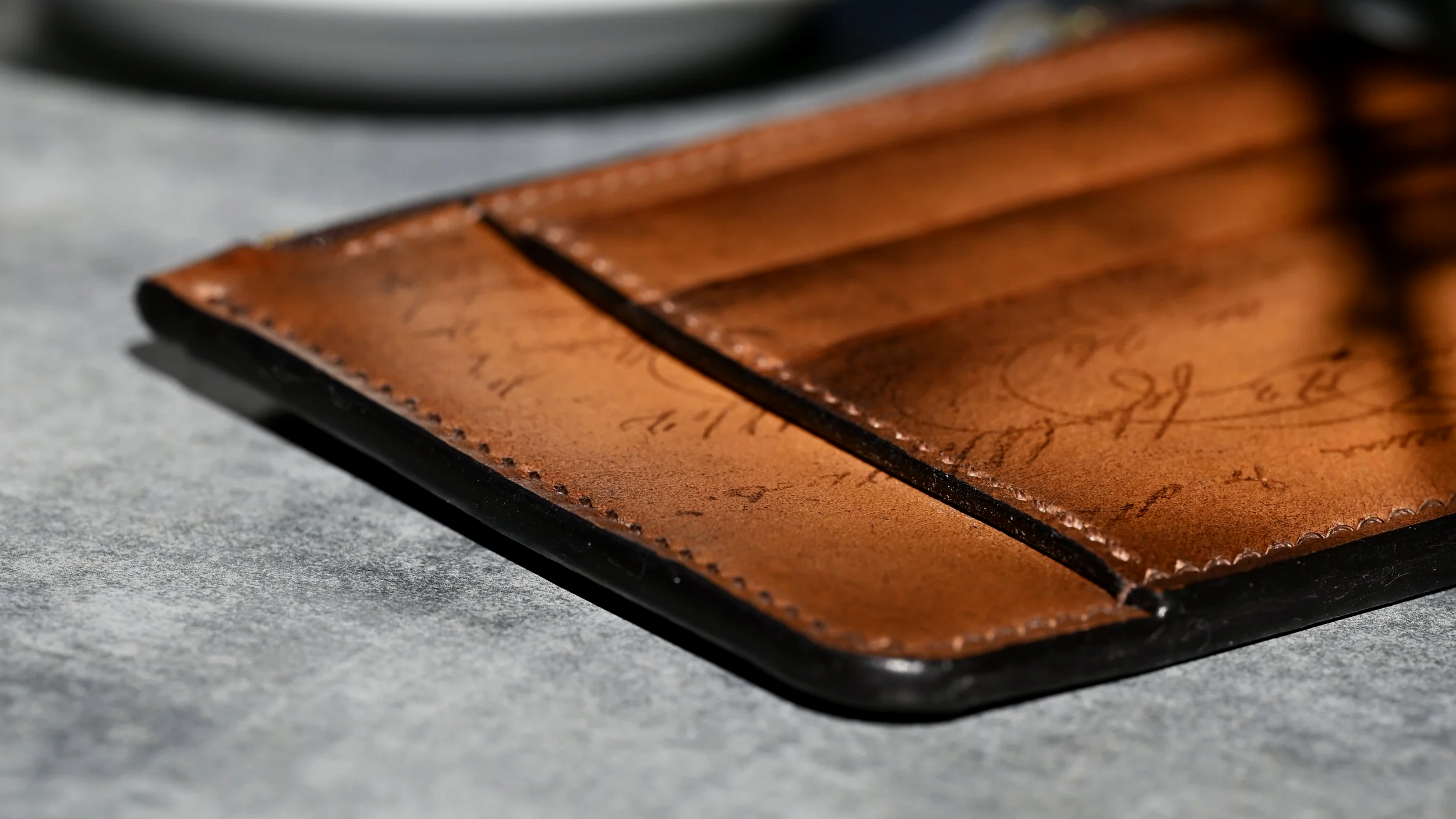 Gros plan sur un porte carte en cuir tanné végétal patiné à la main posé sur un support gris