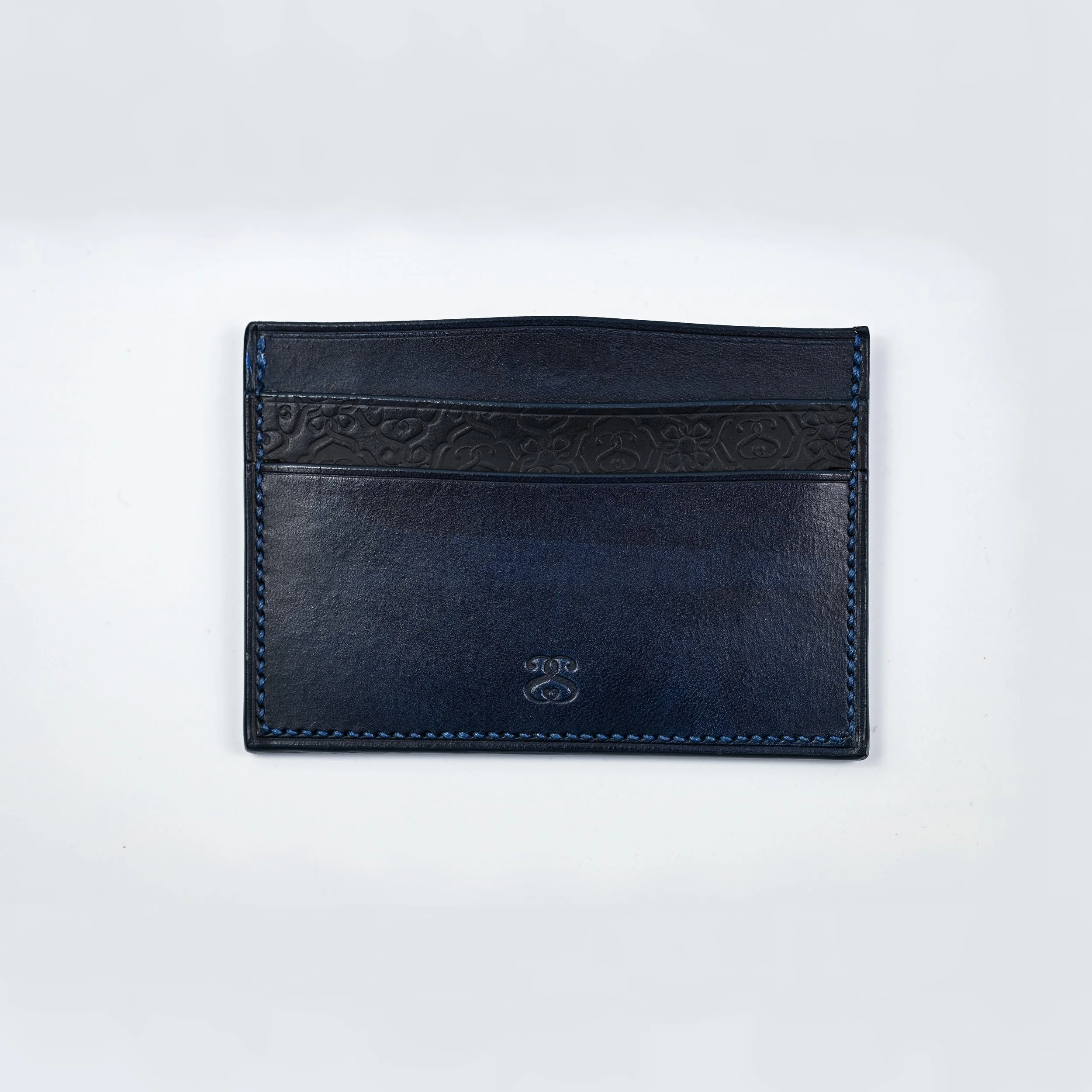 Porte-cartes en cuir bleu avec un motif gravé noir sur le haut et une initiale en relief au centre.