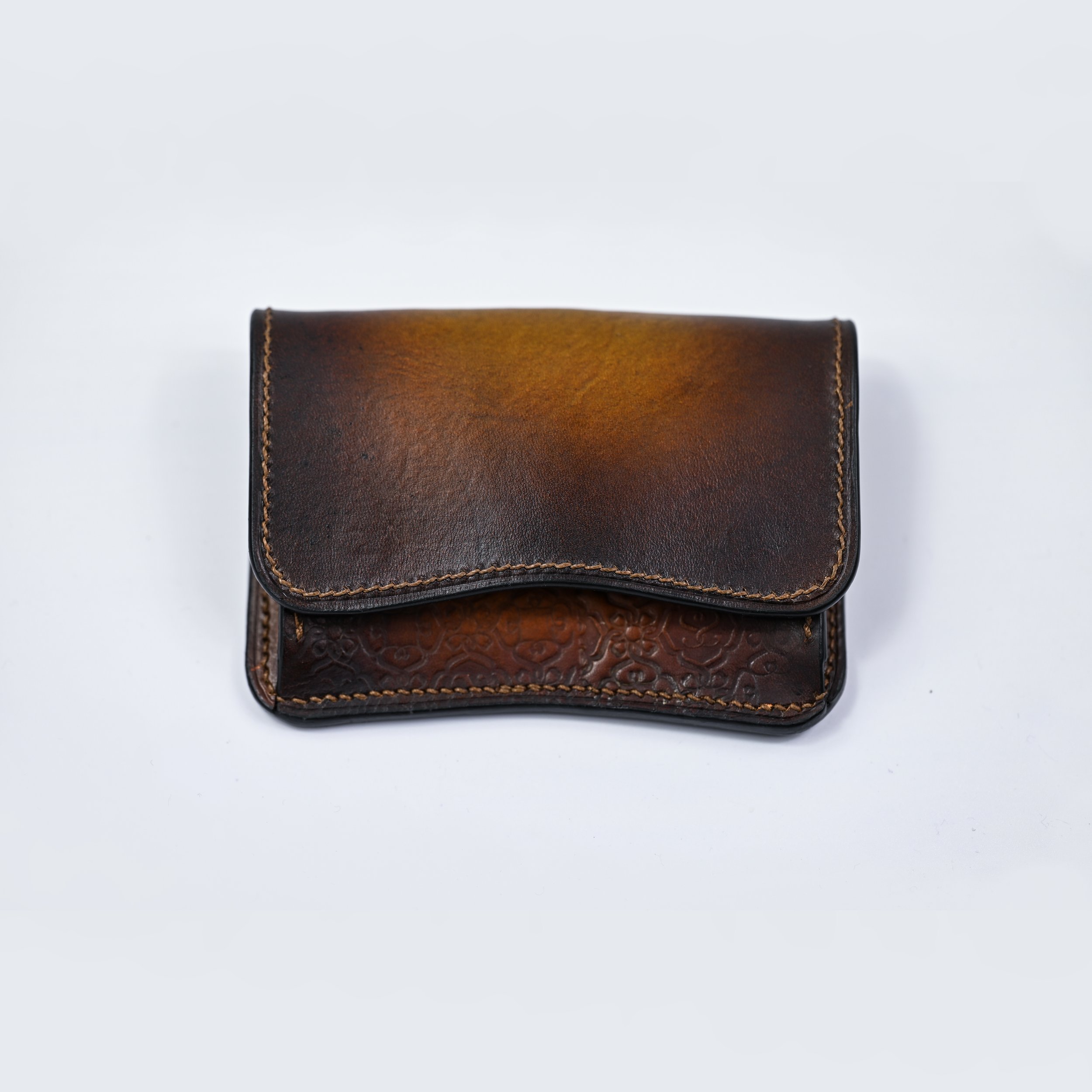 Petit porte-monnaie en cuir marron foncé avec une texture lisse et un motif gravé en bas, posé sur un fond blanc.