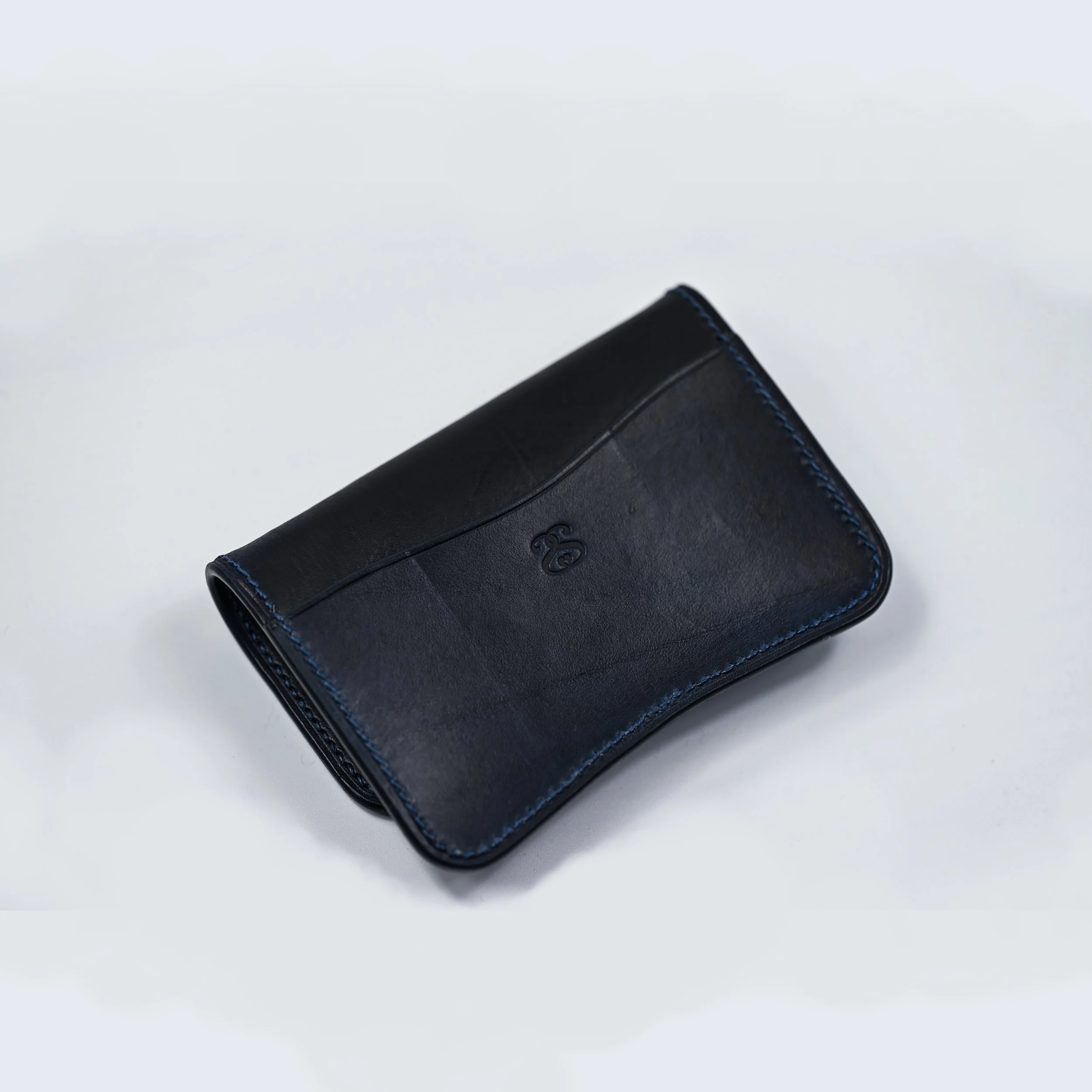 Un portefeuille noir en cuir avec des coutures bleues, posé sur un fond blanc.