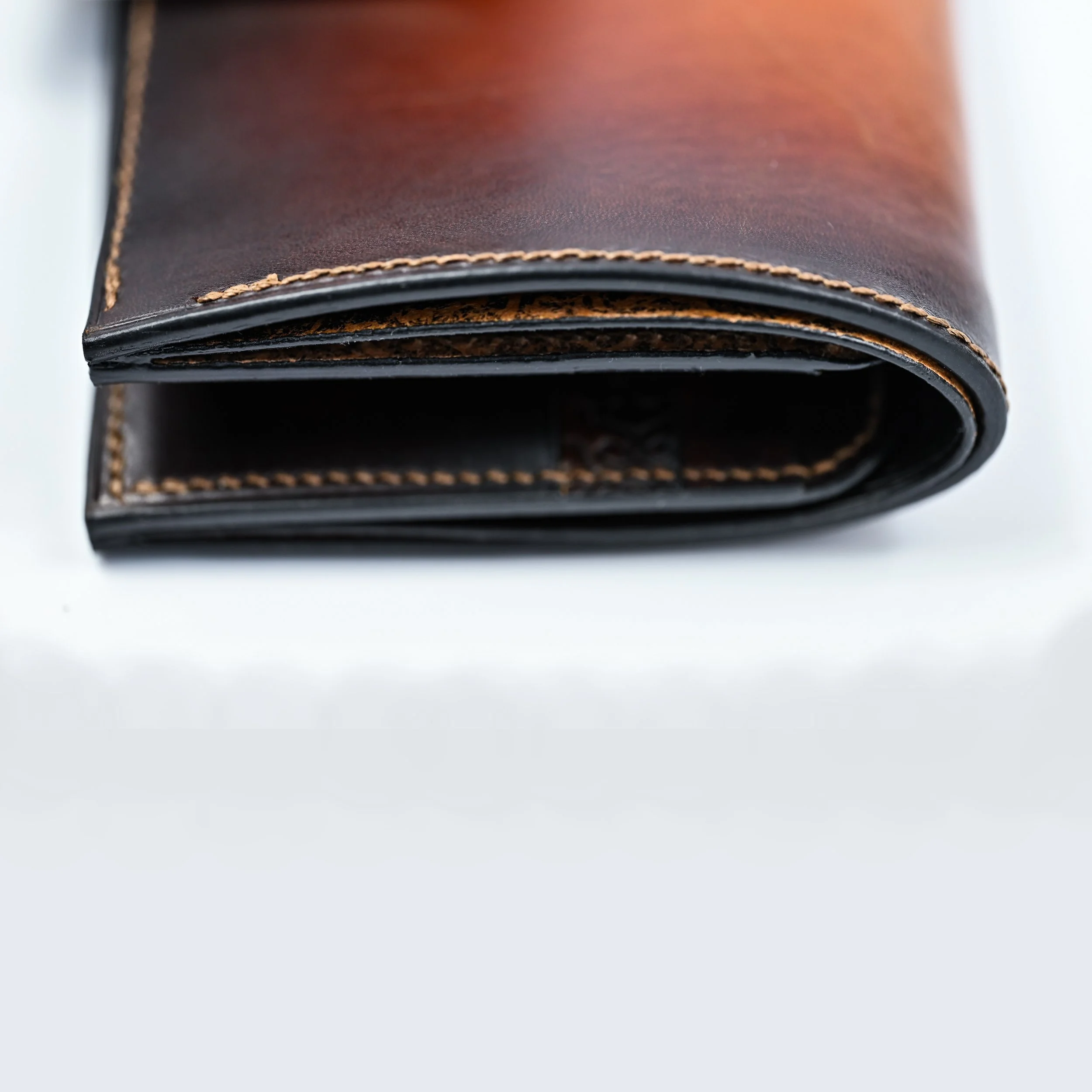 Portefeuille en cuir marron noir, fermé, avec coutures contrastantes, placé sur un fond blanc.