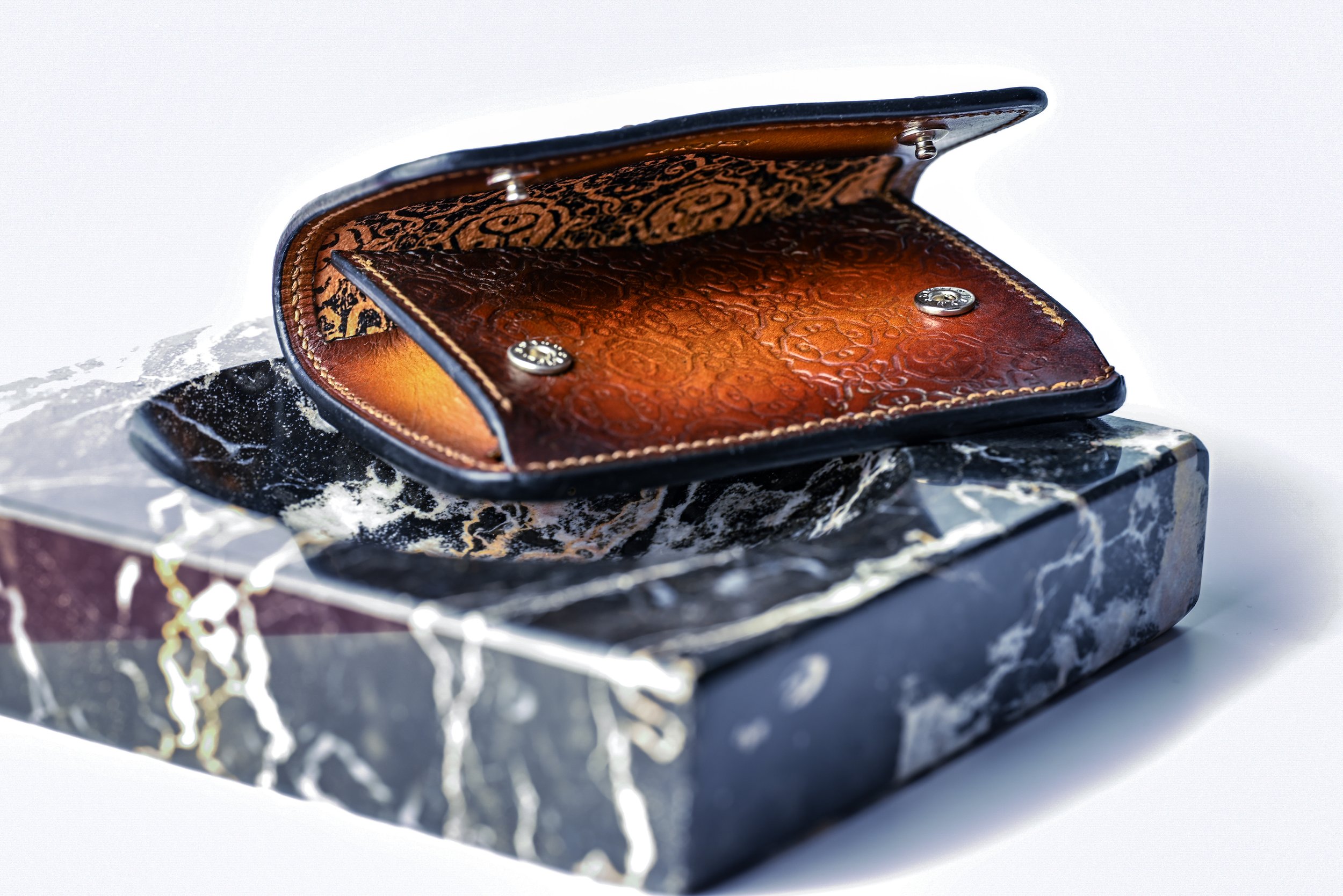 Un portefeuille en cuir marron ouvert posé sur une boîte en marbre noire avec des veines blanches et dorées.