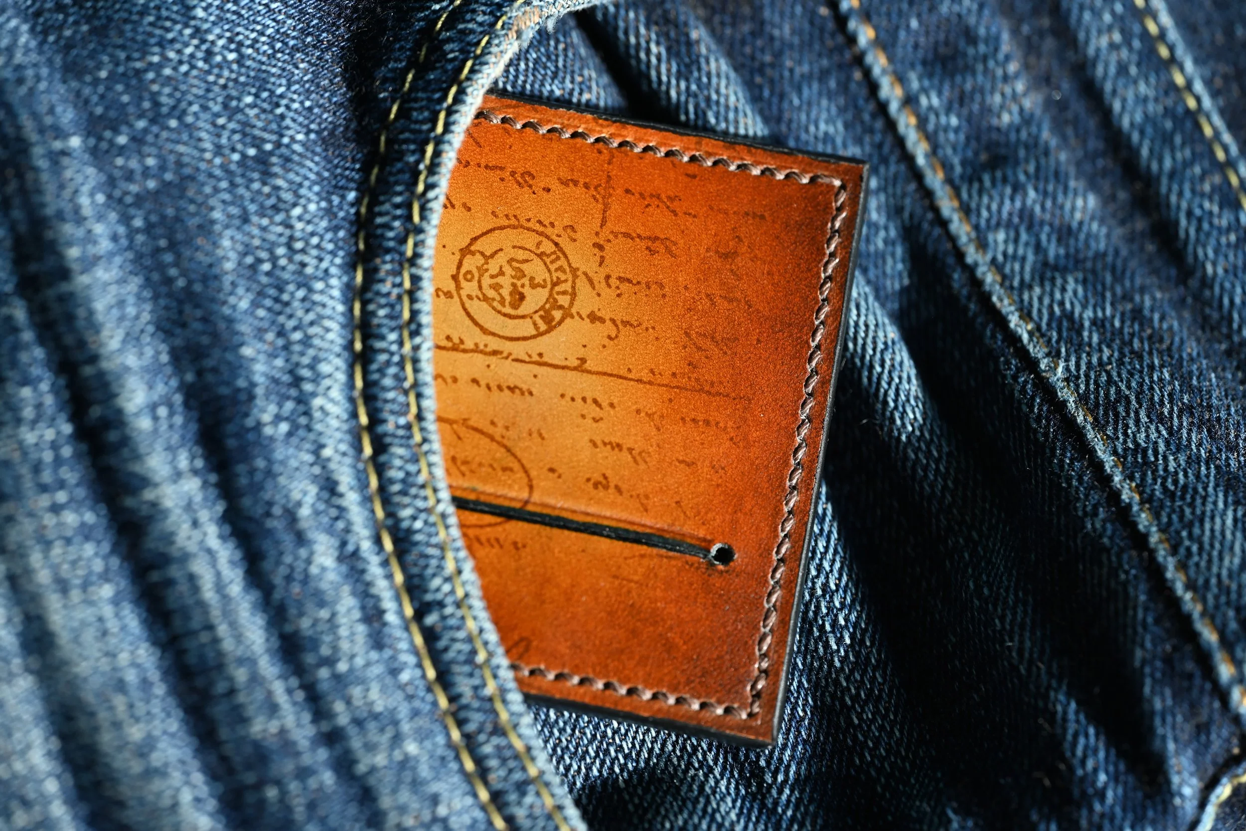 Détail d'une étiquette en cuir orange à l'intérieur d'un jean bleu, cousue sur la poche.