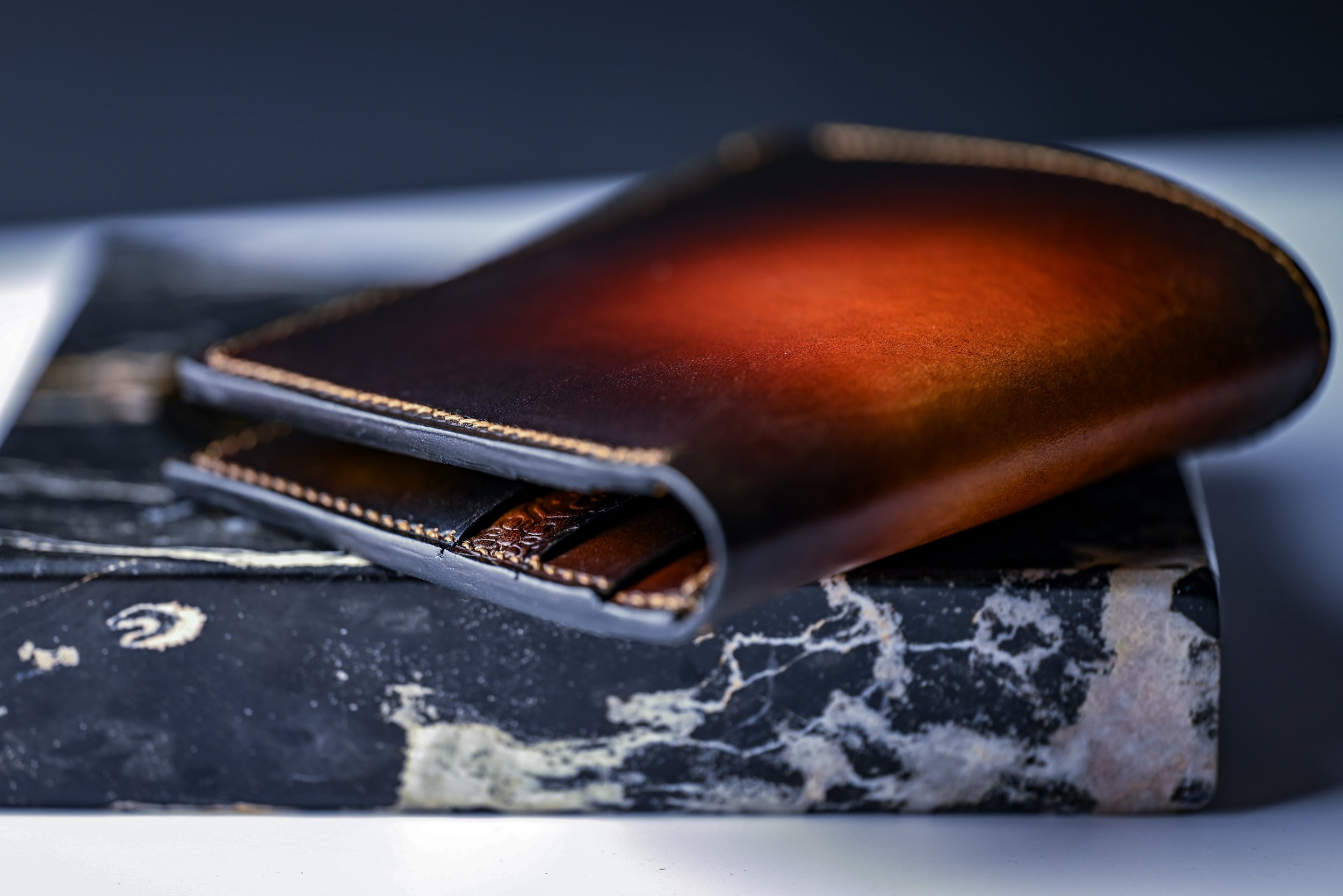 Un portefeuille en cuir marron posée sur un livre en marbre noir.