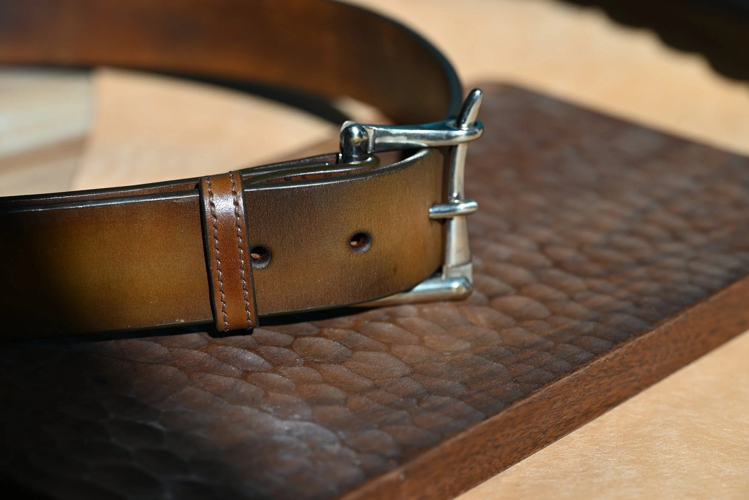 Ceinture en cuir marron avec boucle en métal, posée sur une planche en bois.