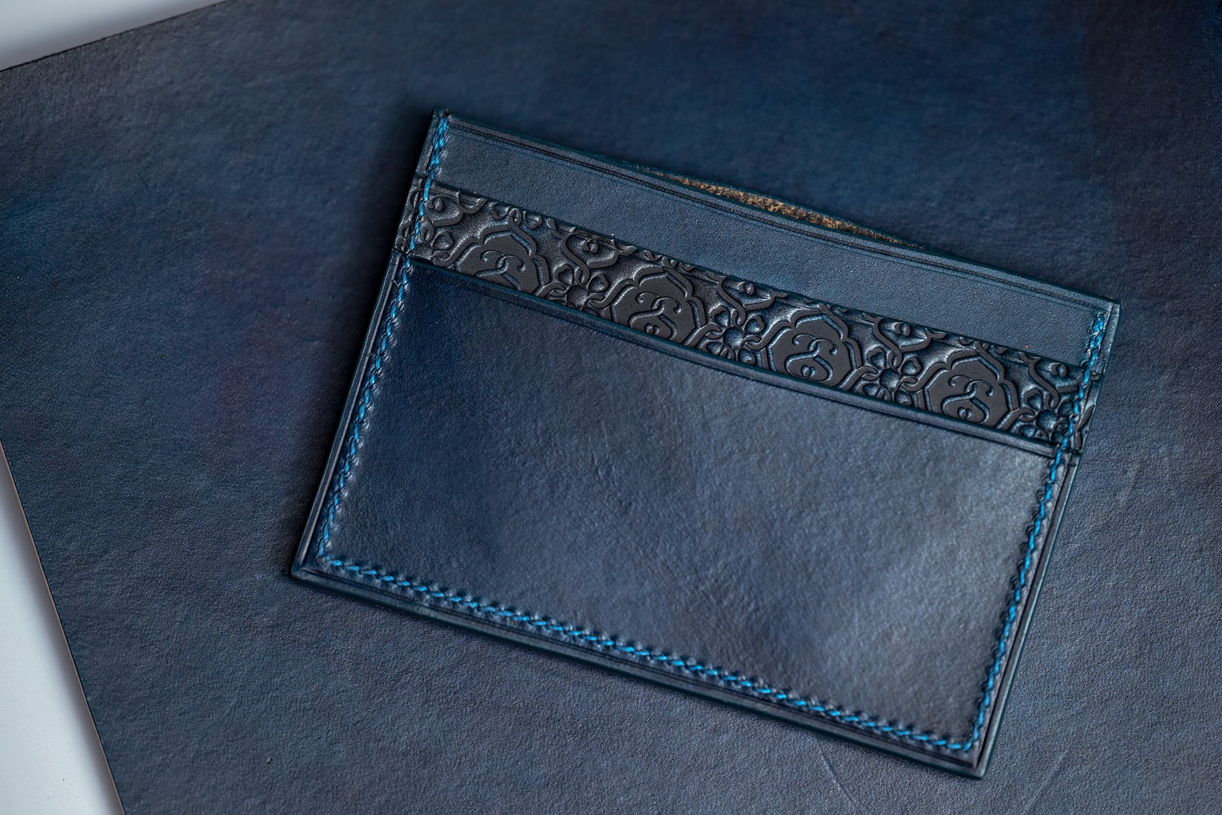 Porte-cartes en cuir teint à l'indigo naturel, motifs embossés main et logo discret, posé sur un cuir indigo