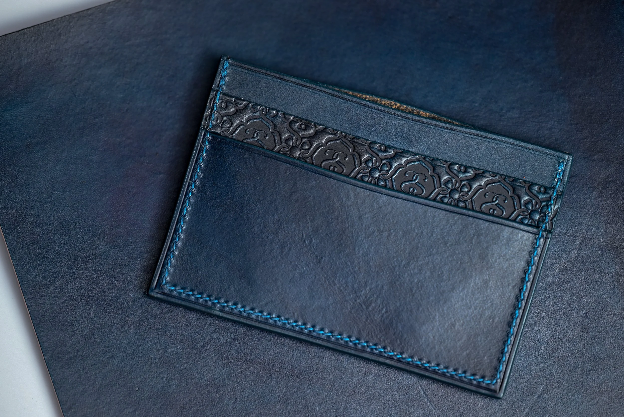 Une pochette en cuir bleu avec une poche en relief noir et des surpiqûres bleues.