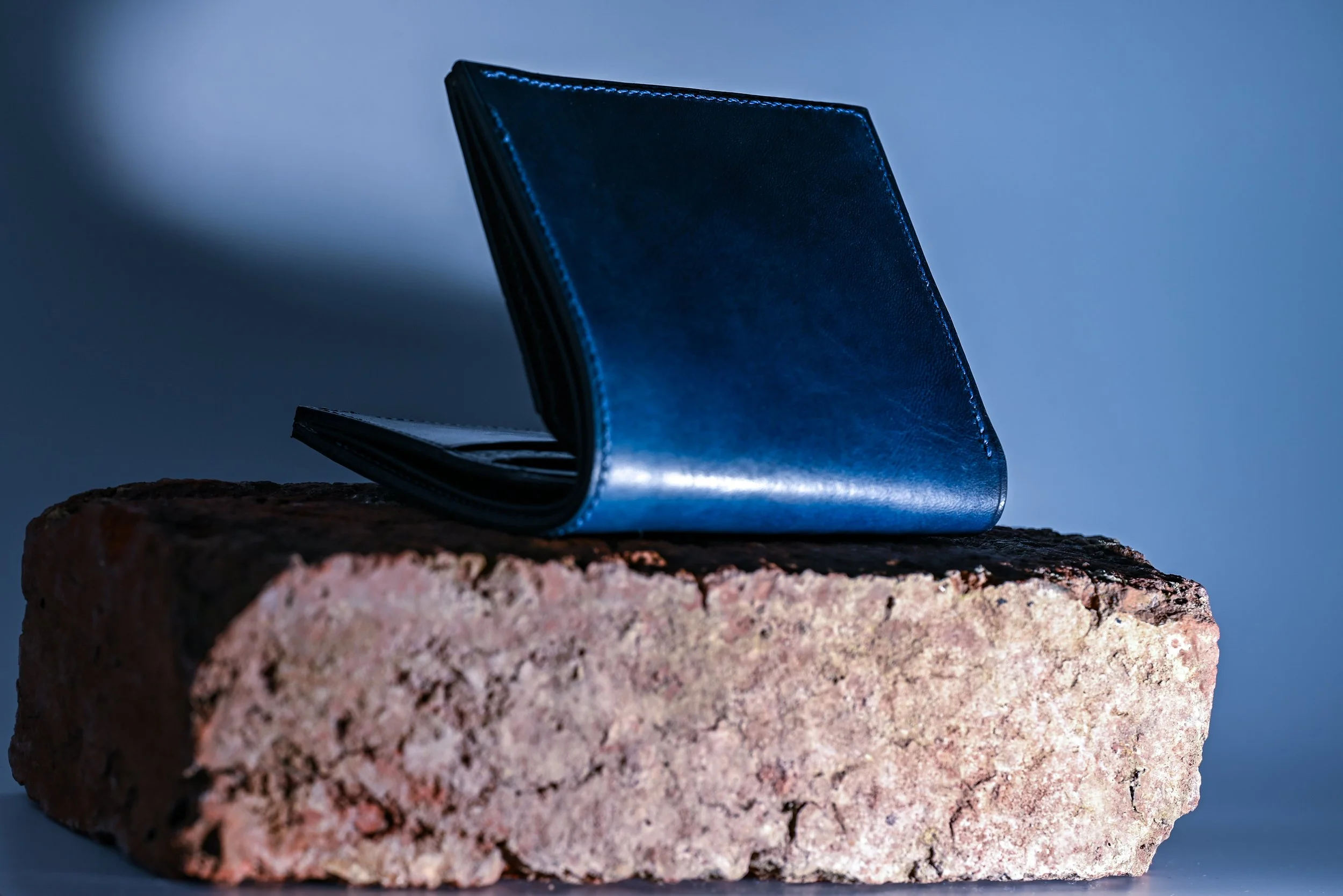 Un portefeuille en cuir bleu posé sur un gros bloc de pierre, avec un fond sombre et une lumière dirigée