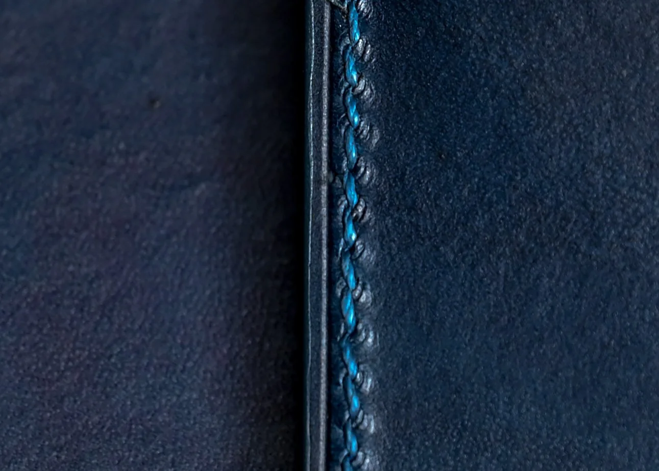 Zoom sur la couture d'un sac ou vêtement en cuir bleu foncé avec du fil bleu brillant.