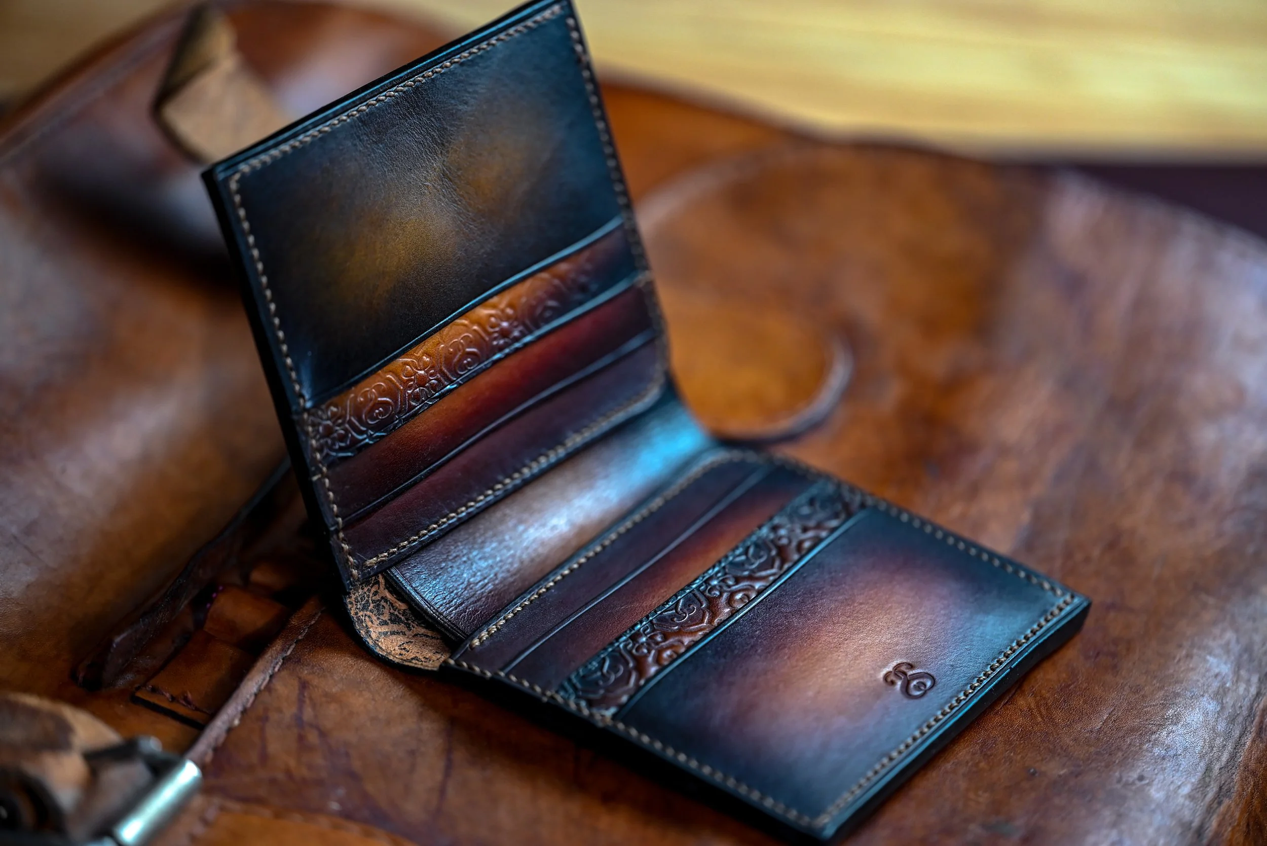 Portefeuille en cuir patiné de la collection Héritage, intérieur à soufflets ouvert, posé sur une sacoche en cuir ancienne des années 1950.