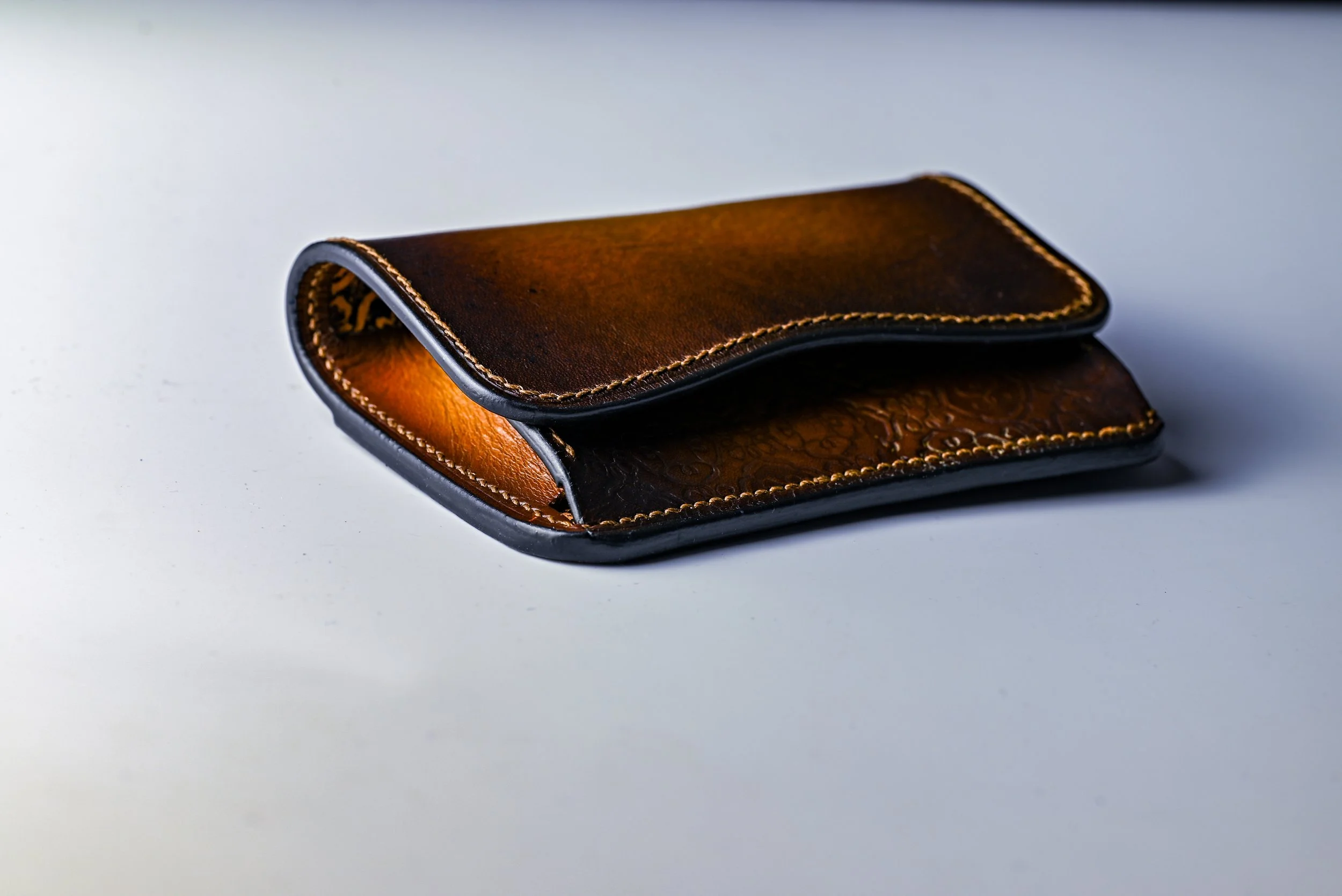 Portefeuille en cuir brun avec couture beige, posé sur une surface blanche.