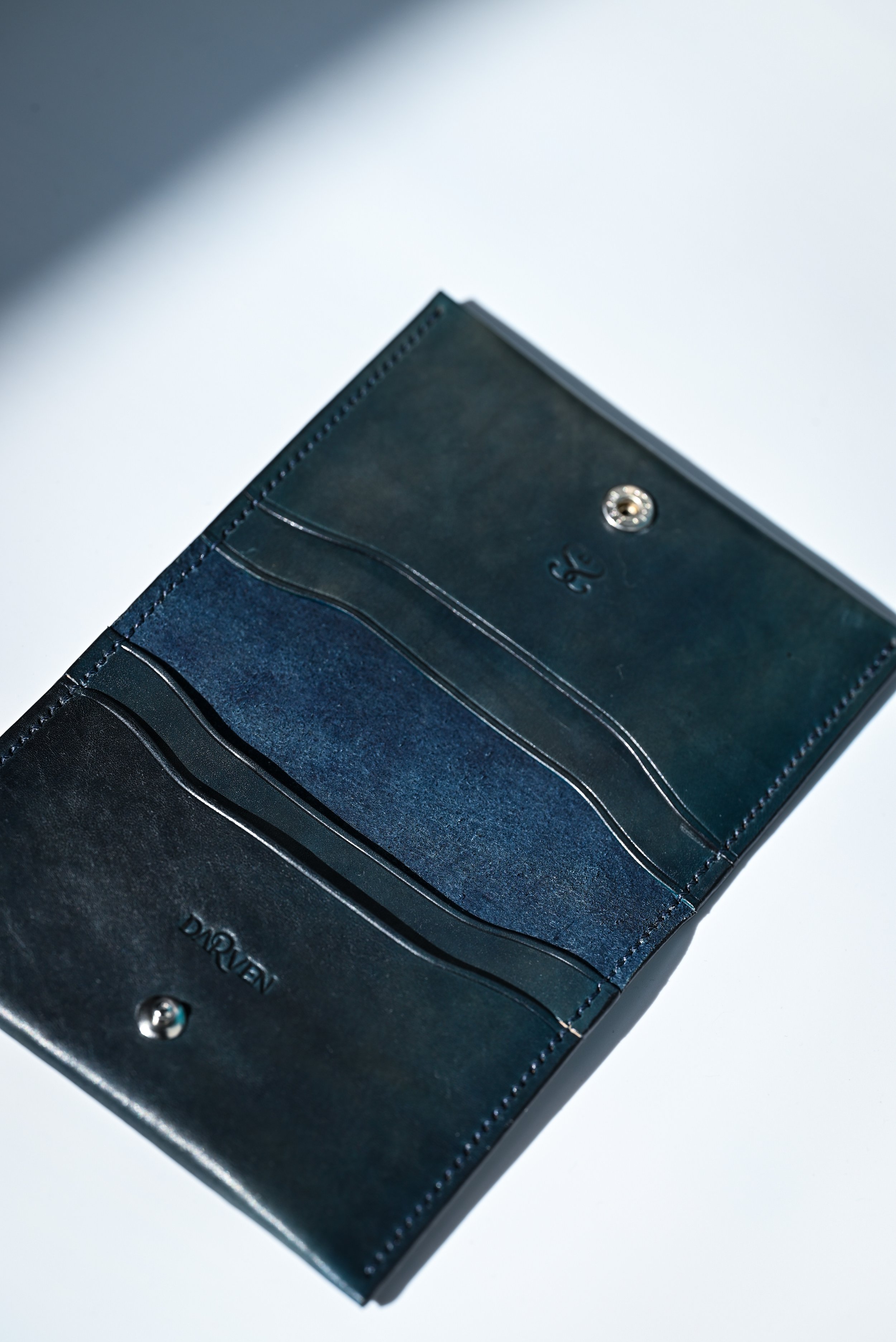 Portefeuille en cuir noir, ouvert, avec plusieurs compartiments, placé sur une surface blanche avec un éclairage partiel.