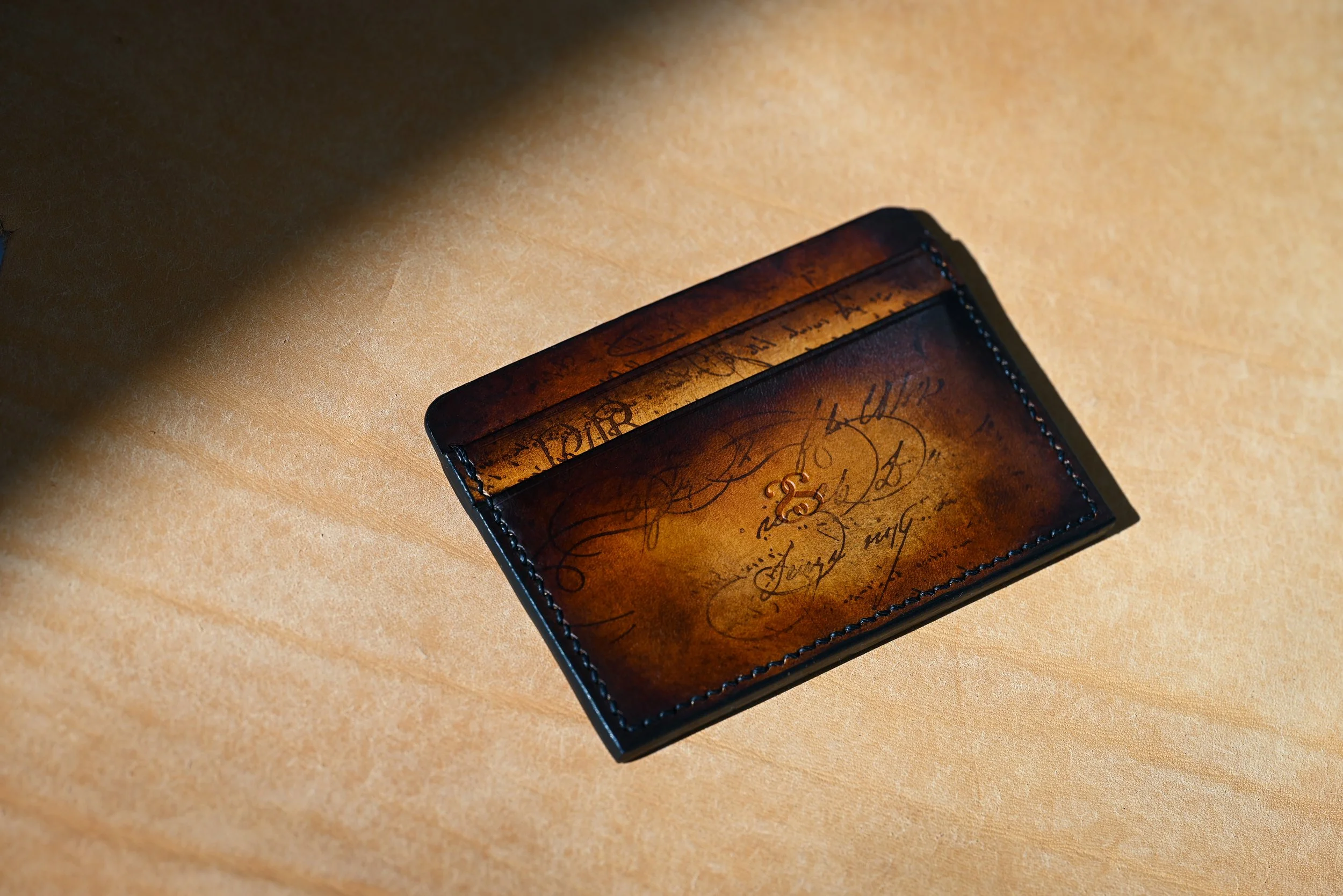 Porte-carte en cuir marron avec écriture calligraphique sur une surface en bois clair.