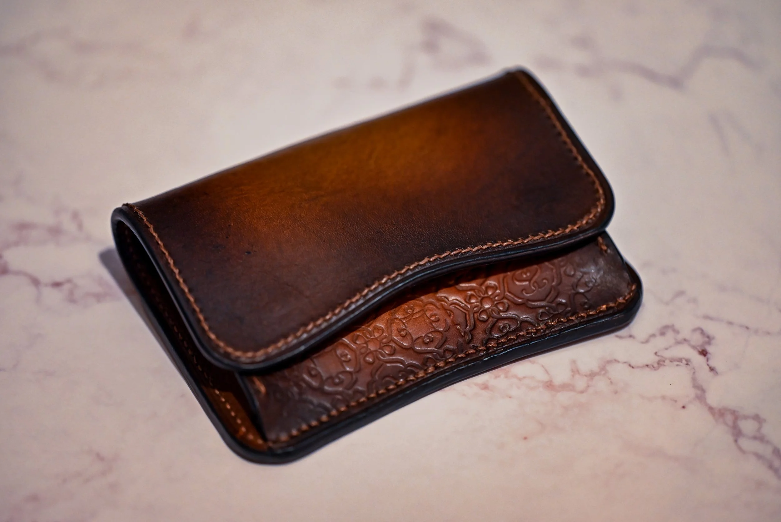 Porte-monnaie de la gamme héritage en cuir patiné à la main. Le porte monnaie est posé sur un support en marbre.