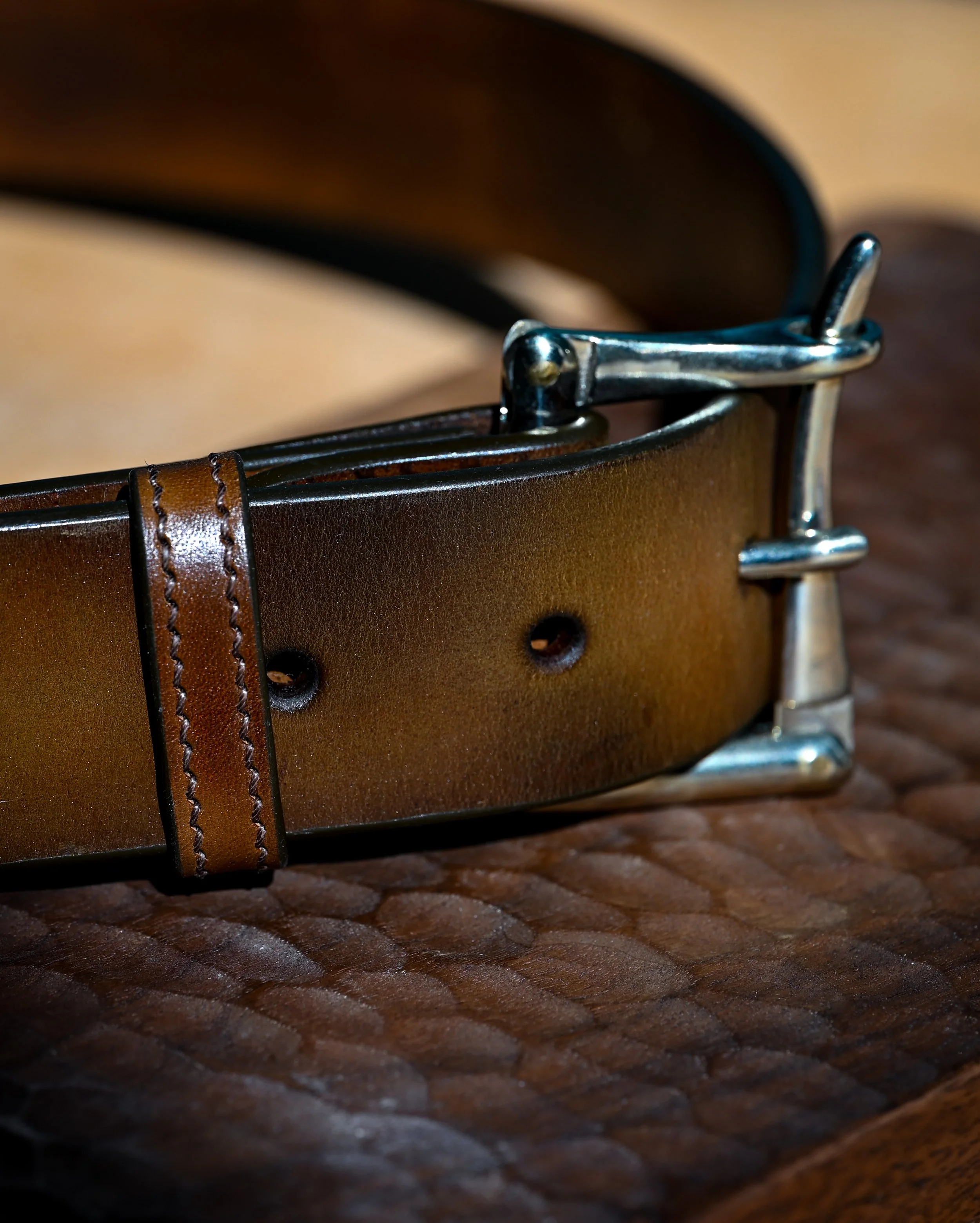 Ceinture en cuir brun avec boucle en métal argenté posée sur une surface en bois texturée.