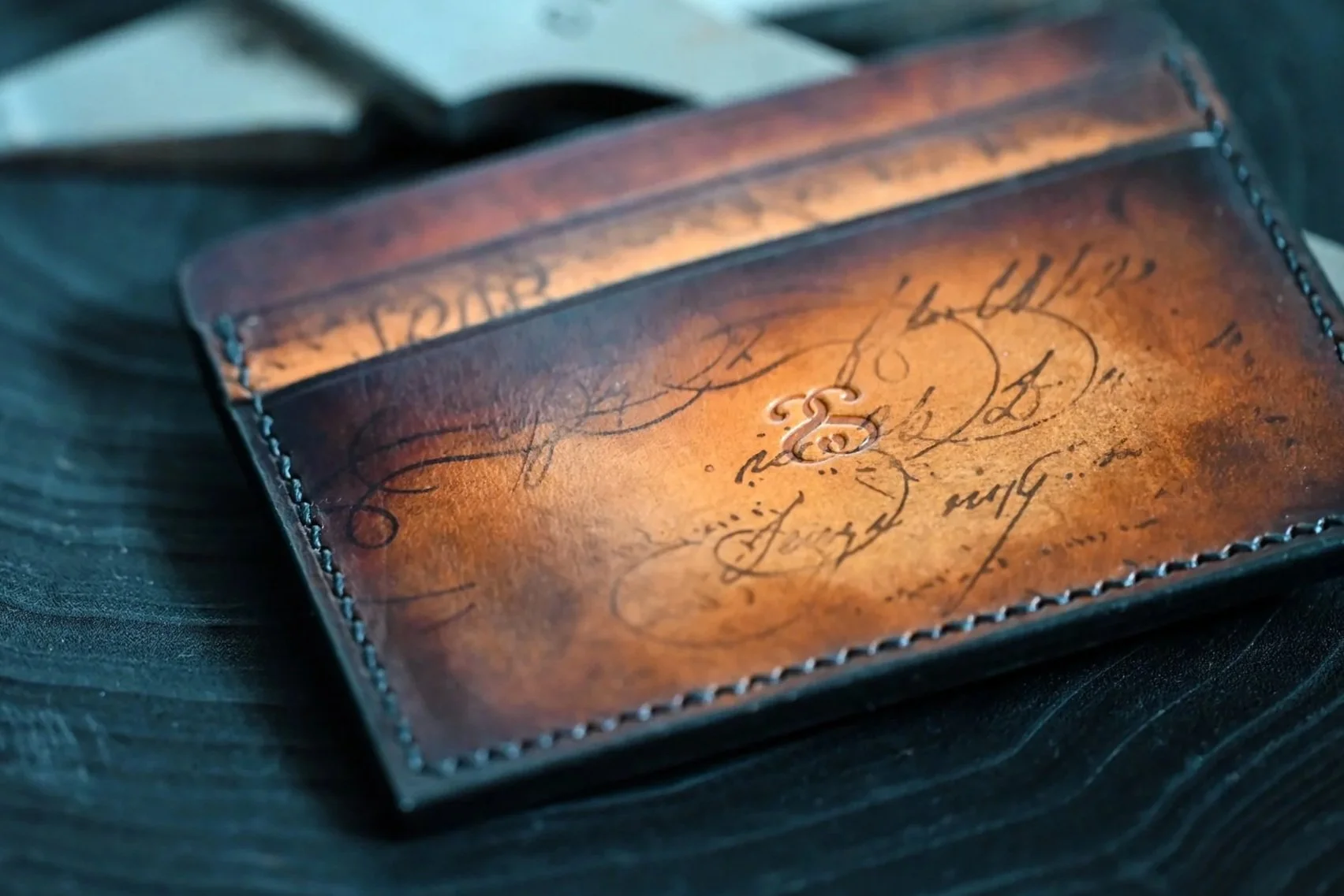 Un porte-carte en cuir tanné végétal patiné posé sur un morceau de bois noir