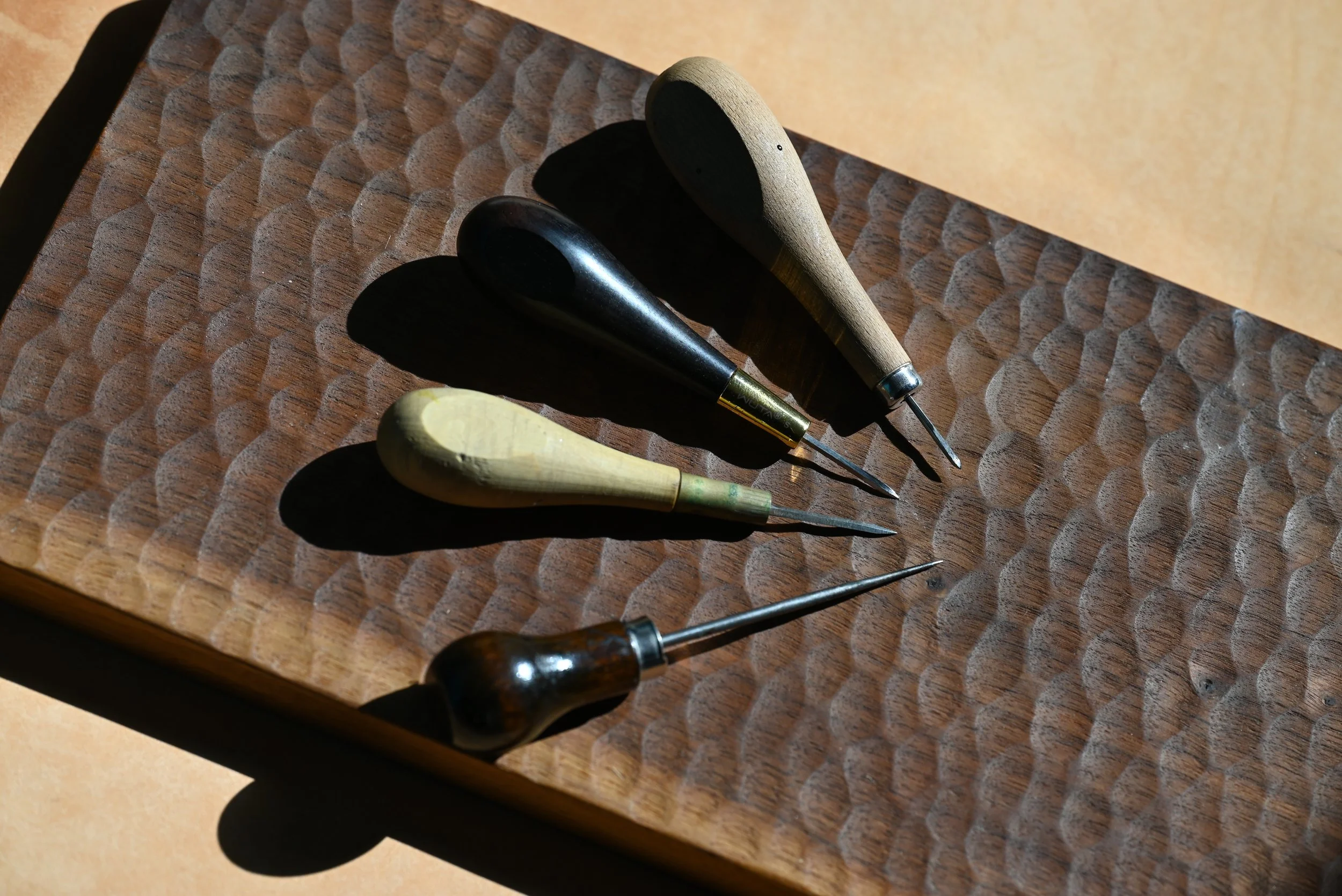 Cinq outils de bricolage en bois placés sur une surface en bois avec empreintes circulaires, sous une lumière naturelle.