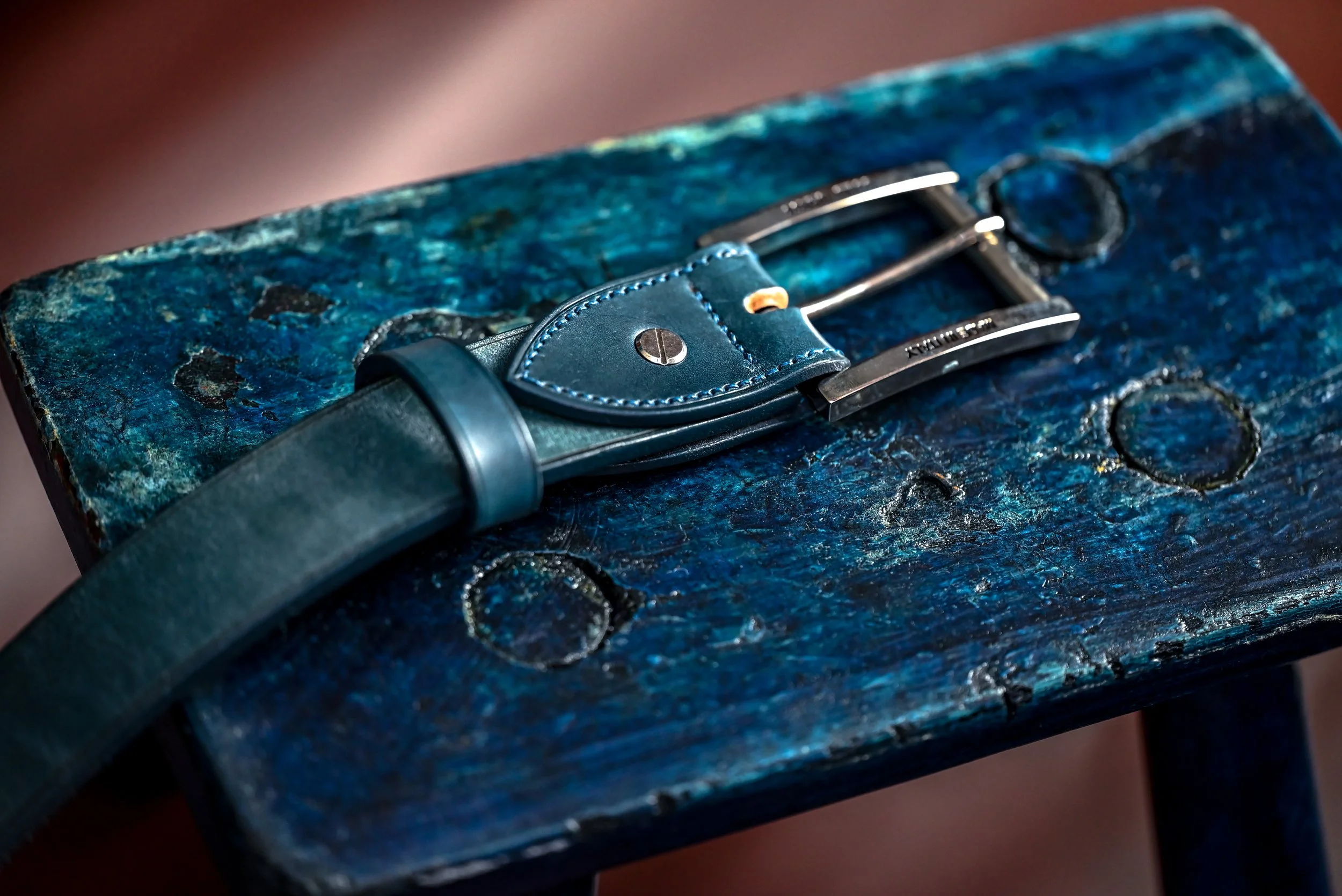 Un couteau de cuisine en acier avec un manche en cuir bleu, posé sur une surface en bois peinte en bleu délavé.