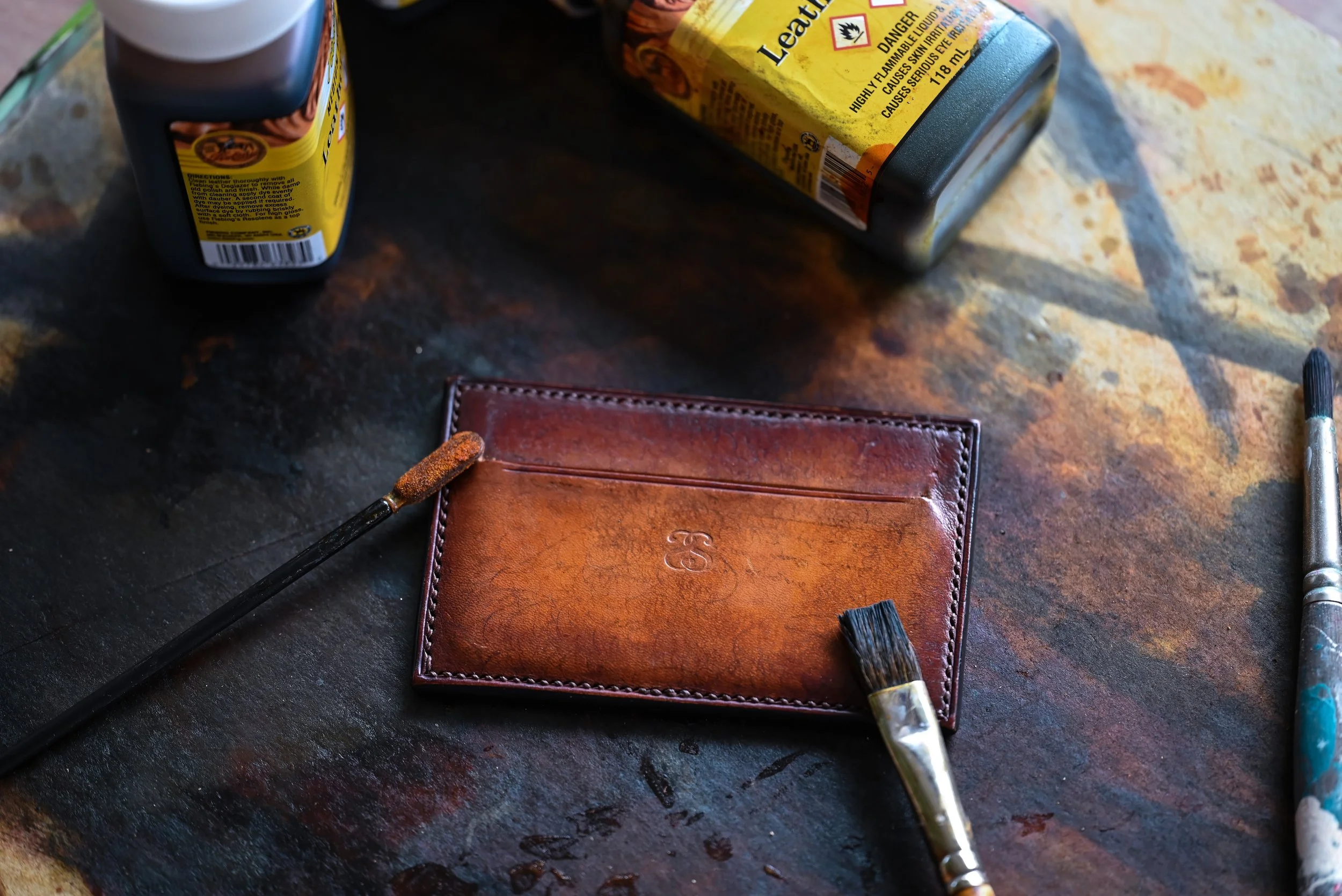Une surface en pierre avec une portefeuille en cuir, deux pinceaux, un bidon de liquide de nettoyage et un bidon d'huile, tous liés à la réparation ou à l'entretien du portefeuille.