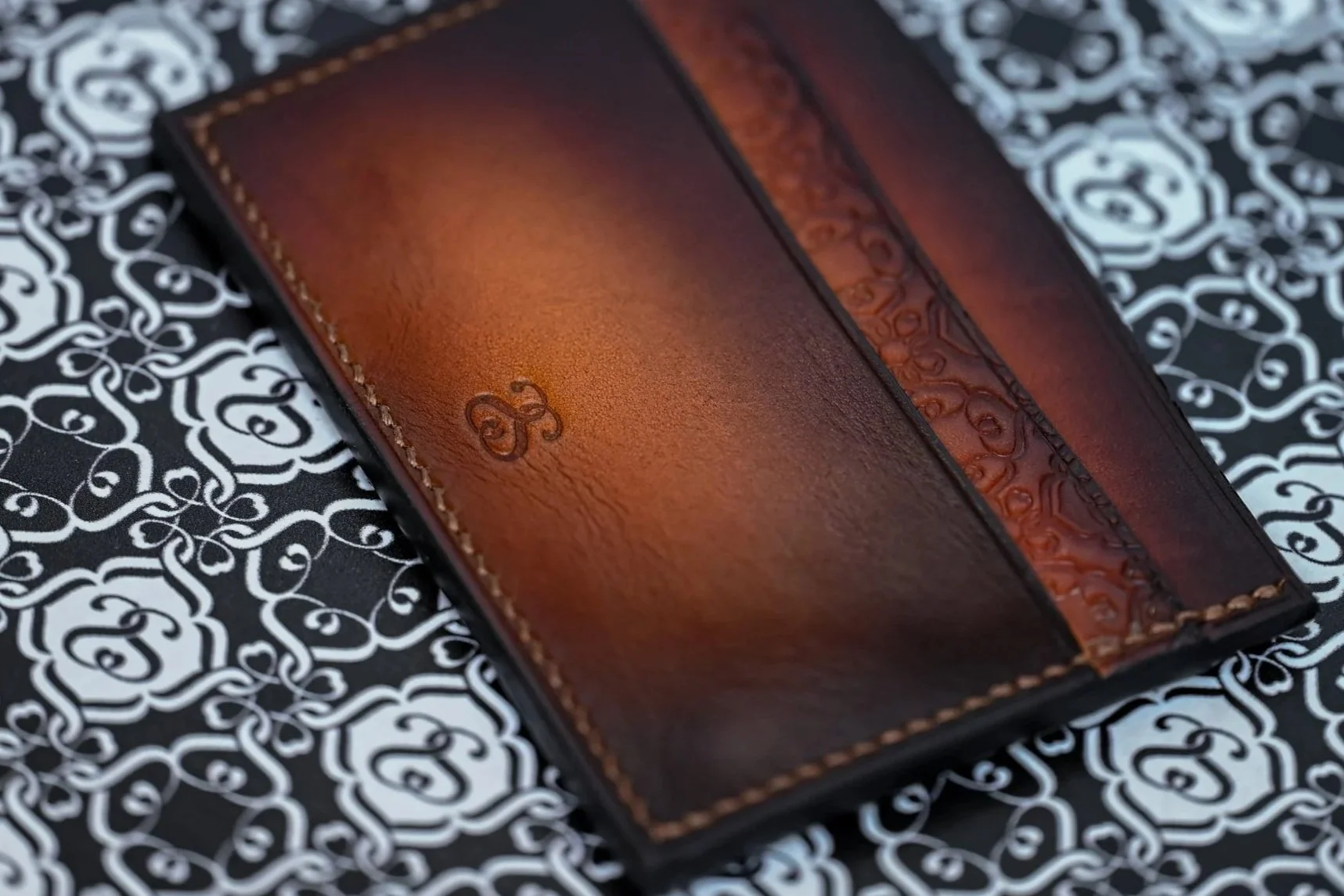 Gros plan sur un porte-carte en cuir tanné végétal patiné avec une couture point sellier posé sur un support avec monogramme