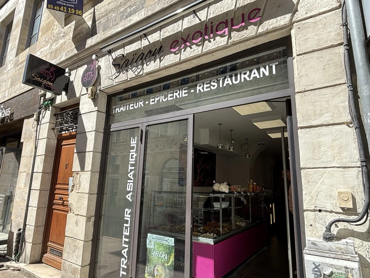 Façade d'une boutique proposant des produits traiteur, épicerie et restaurant, avec une enseigne indiquant 'Saïgan exotique' et un panneau à gauche 'TRAITEUR ASIATIQUE'.