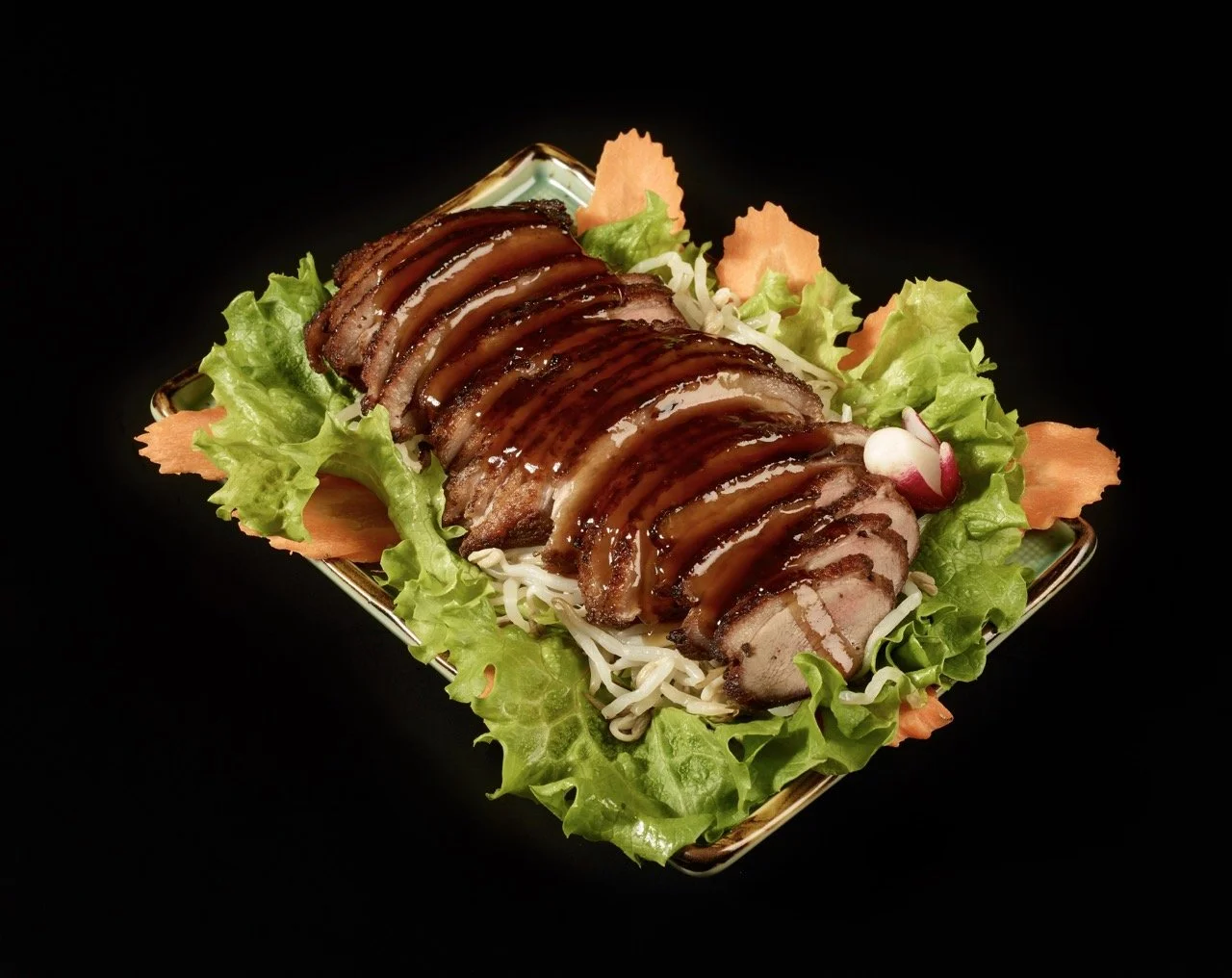 Plat de viande en tranches nappée de sauce, présenté sur un lit de salade verte et de julienne de légumes, dans une assiette carrée