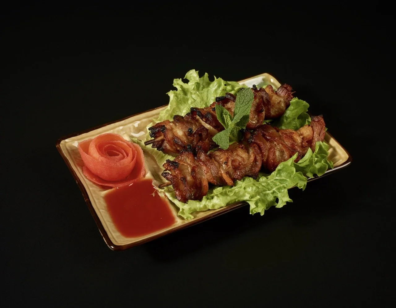 Brochettes de viande grillée sur lit de laitue, accompagnées de rose en viande ou tomate et sauce soja sur une assiette