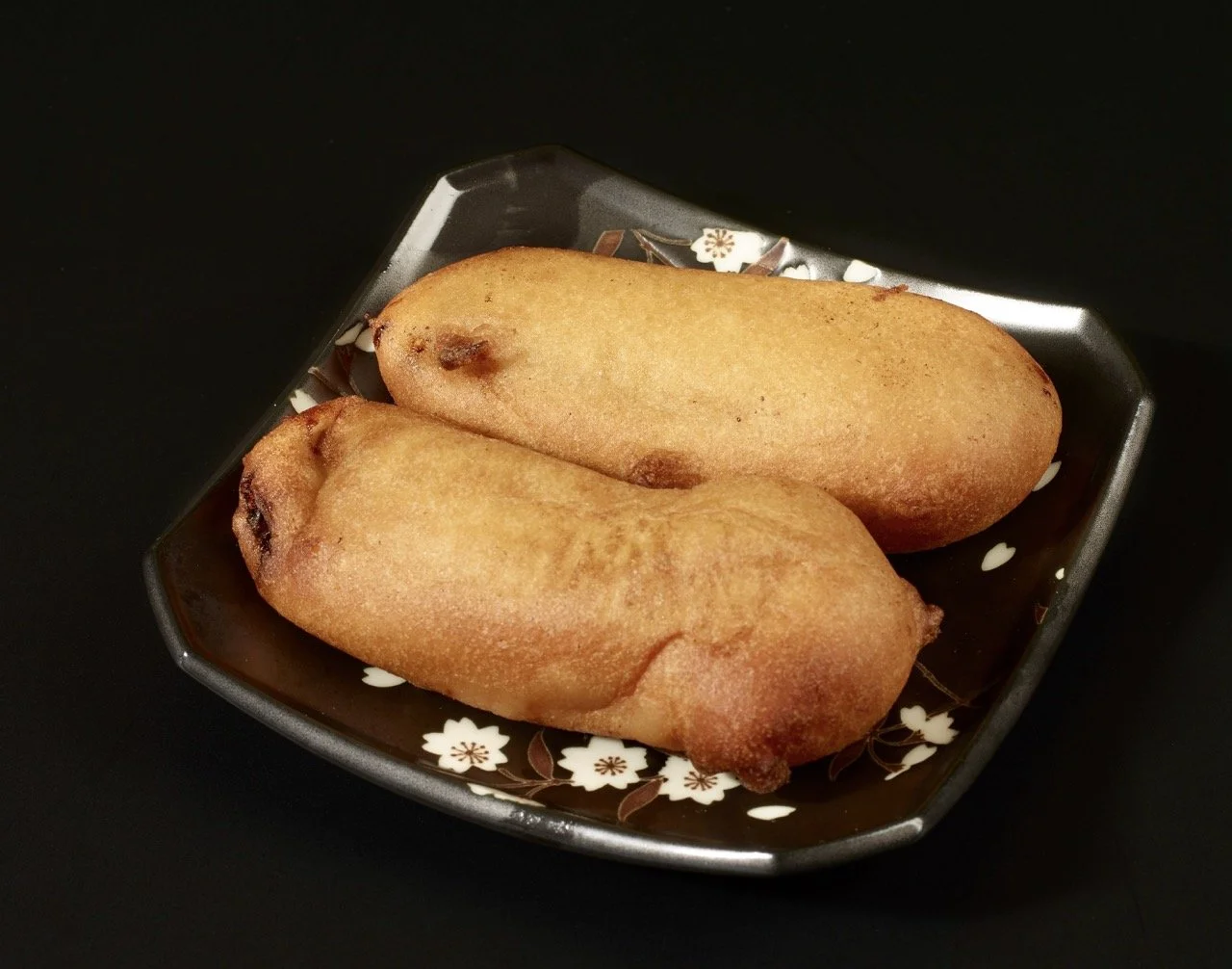 Deux beignets dans un plat noir avec un motif floral blanc.