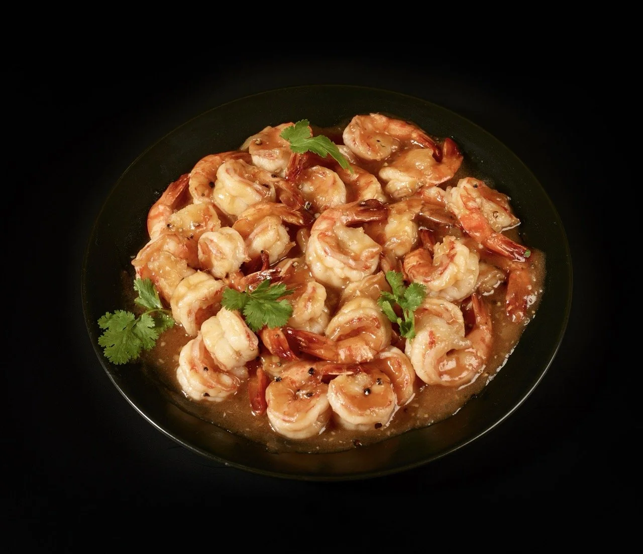 Plate de crevettes sautées garnie de coriandre fraîche, sur fond noir.