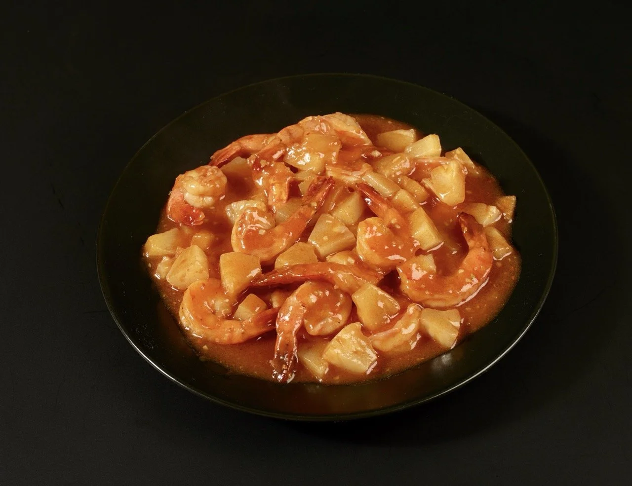 Gambas sautées avec morceaux d'ananas dans une sauce tomate dans un bol noir.