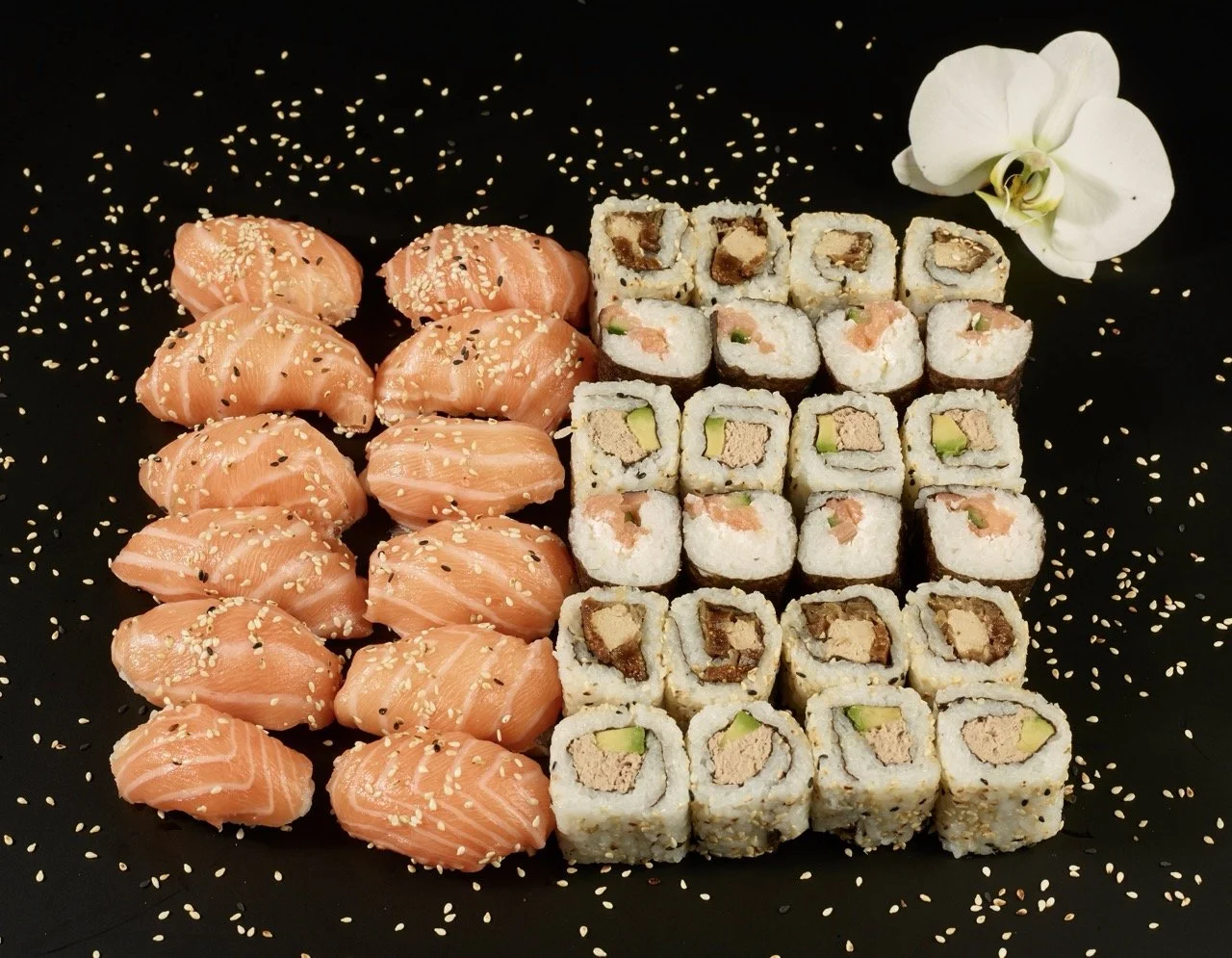 Assortiment de sushis avec du saumon, des rouleaux et un orchidée blanche sur fond noir