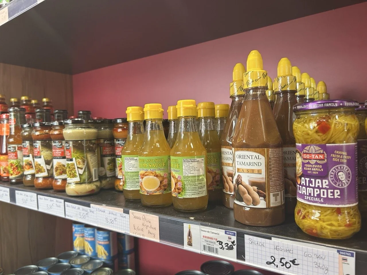 Épicerie asiatique avec des sauces dans des bouteilles en plastique dans un supermarché, notamment de la sauce tamarin, de la sauce aux prunes, et des pickles de légumes.