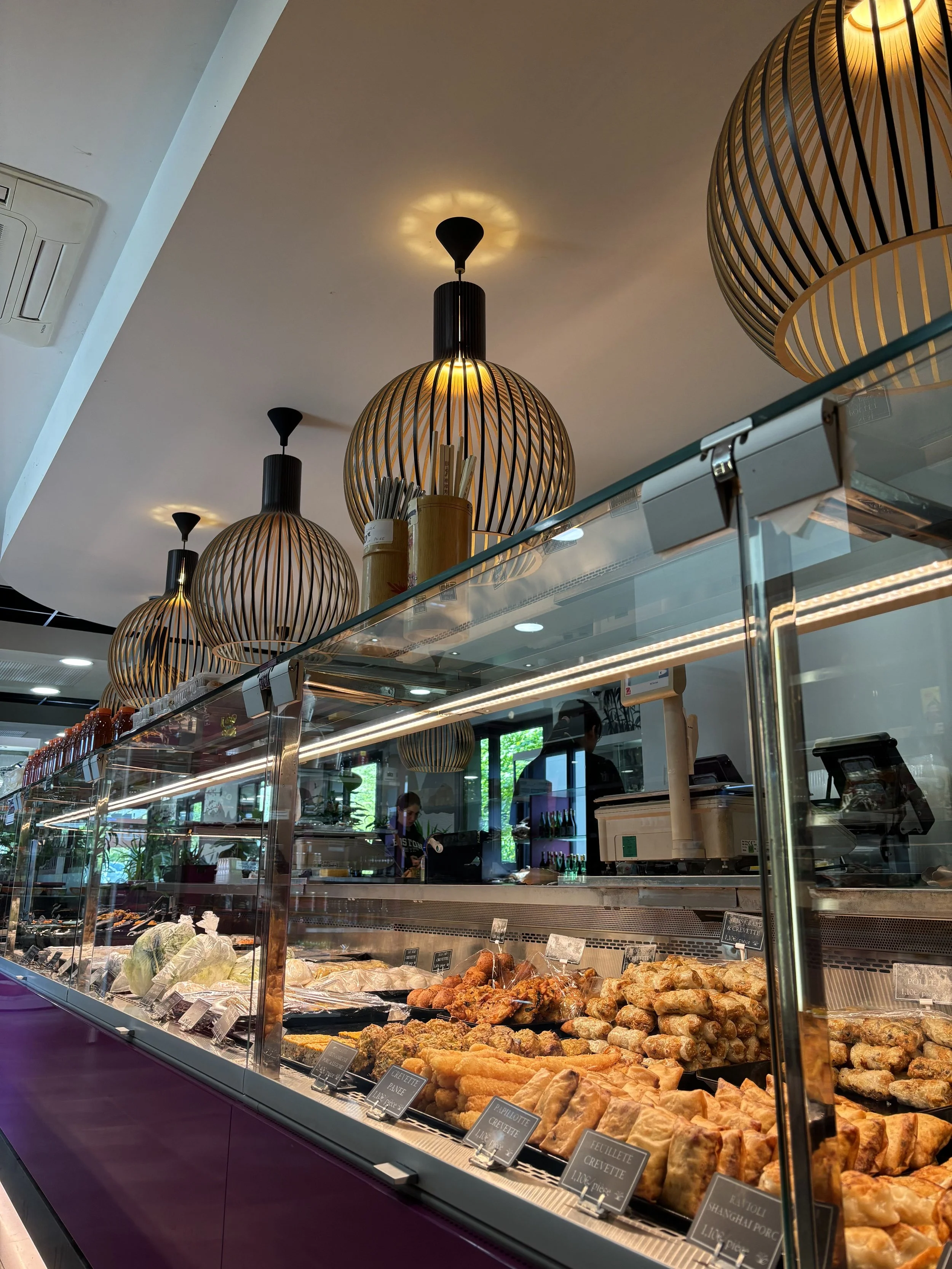 Vitrine de plats de pâtisserie et de snacks dans une bakery ou un café, avec plusieurs lampes suspendues au plafond.