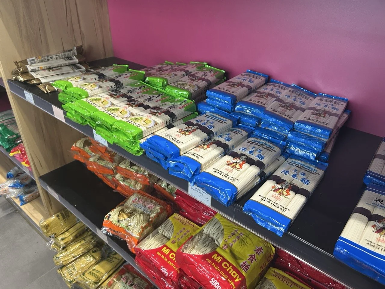 Divers paquets de nouilles instantanées empilés sur une étagère en magasin, avec différentes couleurs et marques