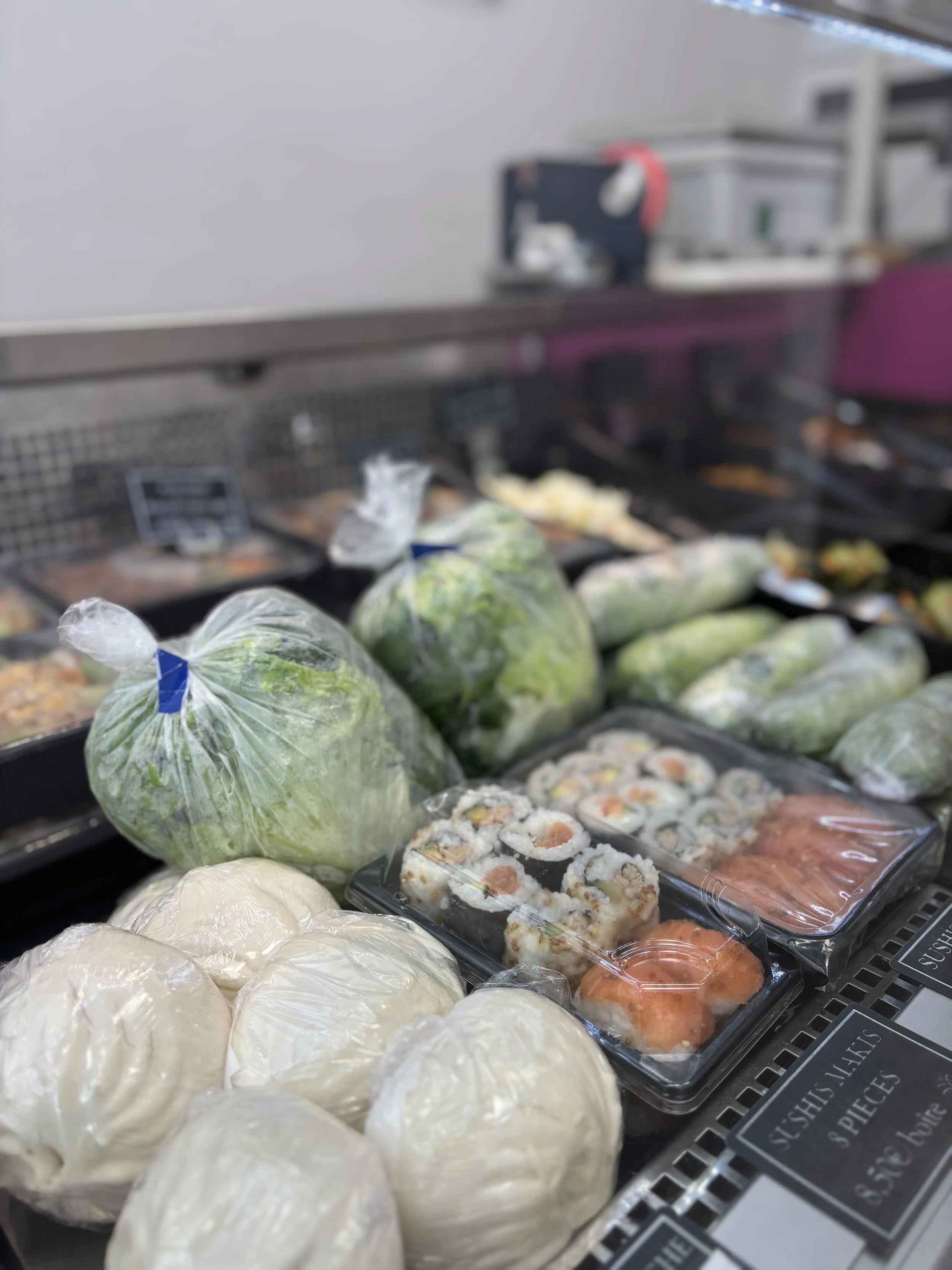 Assortiment de sushis et légumes frais emballés, exposés dans un supermarché.