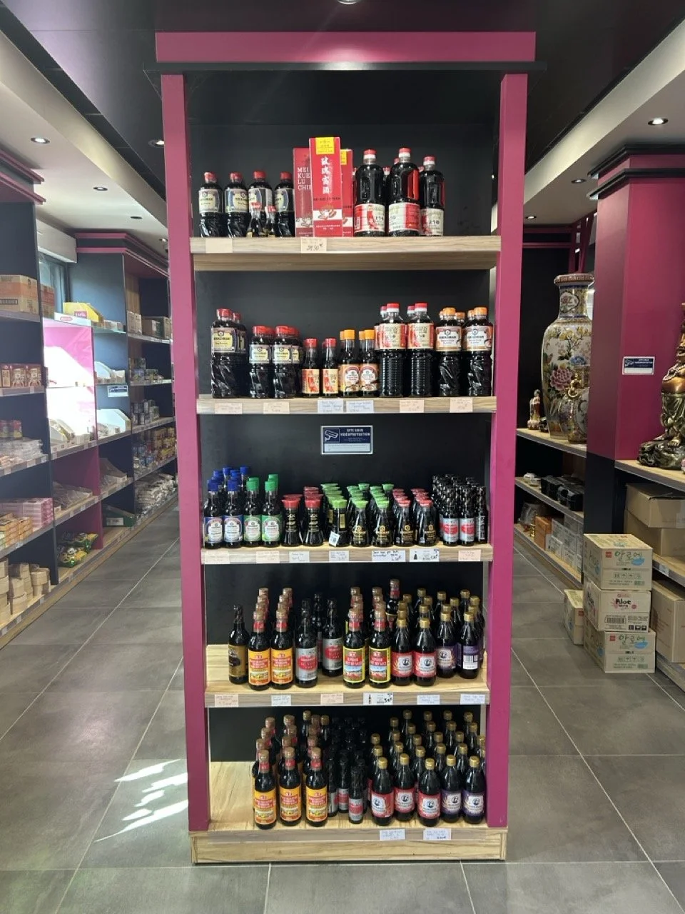 Étagère pleine de bouteilles de sauce soja dans un magasin, avec des étagères voisines contenant d'autres produits.