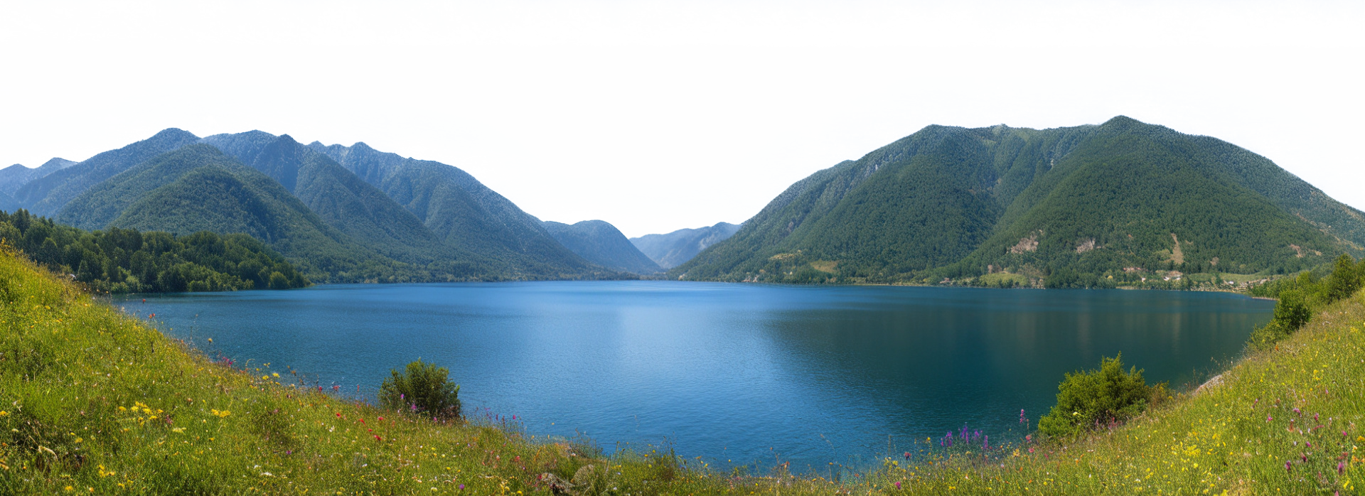 Scenic landscape of a lake surrounded by green mountains under a clear blue sky.