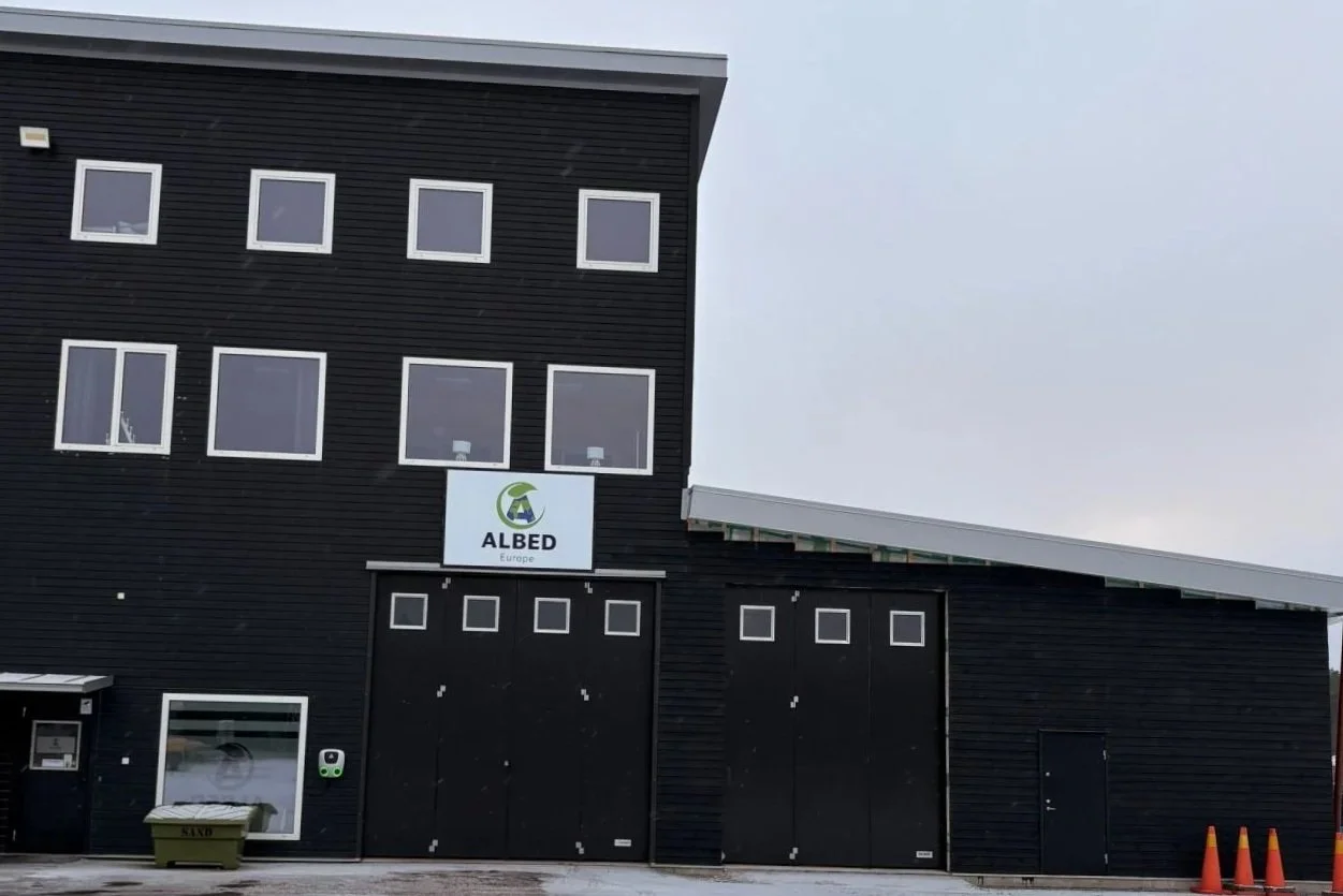Black building with multiple windows and a sign that reads "ALBED Europe" in the center, with garage doors and orange traffic cones in front.