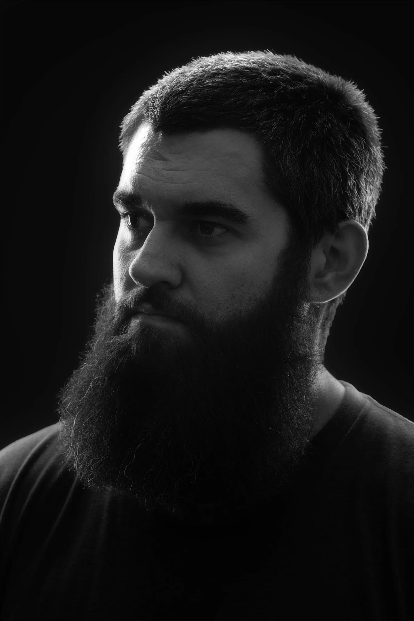 Black and white portrait of a man with a beard and short hair, looking to the side against a dark background.