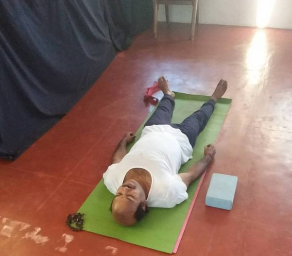 A man lying on his back on a green yoga mat in a room with wooden floors.