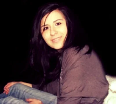 A woman with long dark hair smiling and sitting against a black background.