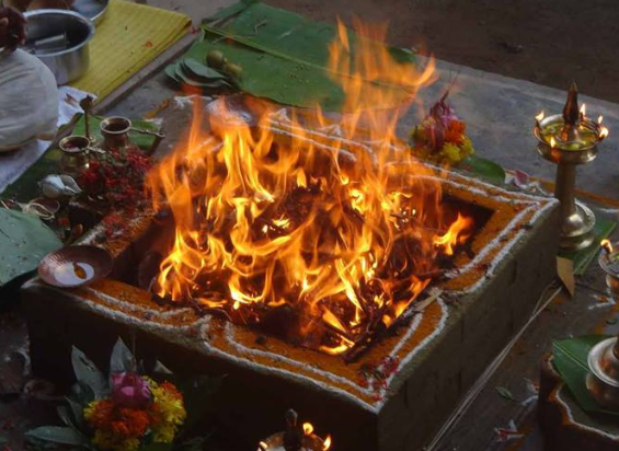 A traditional Hindu funeral fire altar with flames, decorated with flowers, placed on a stone platform, with offerings and religious items surrounding it.