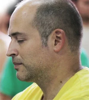 Profile of a man with a shaved head and closed eyes, wearing a yellow shirt.
