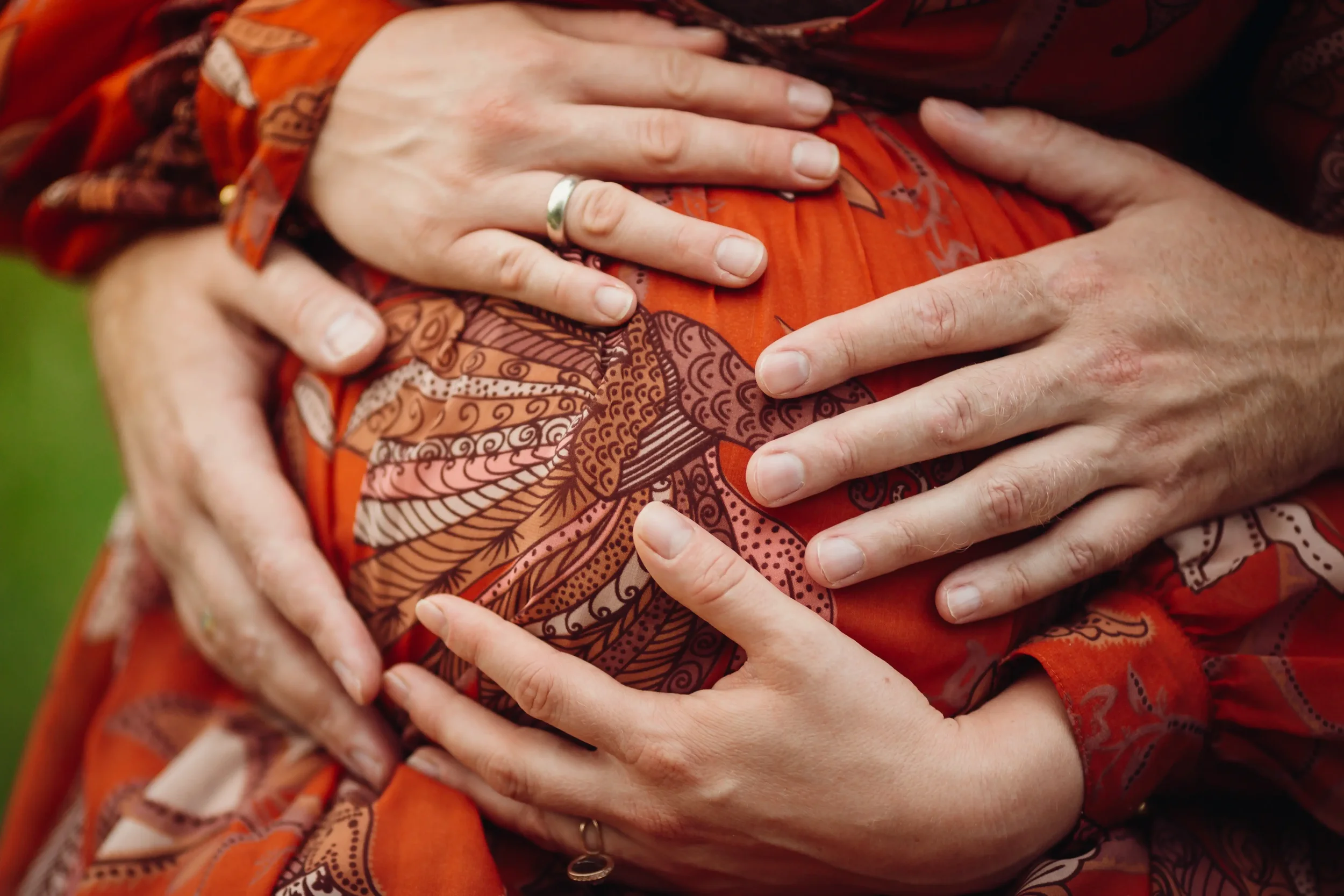 Several hands, including a woman's and a man's, are placed on an orange patterned fabric, symbolizing a close connection, with a ring on the woman's finger.