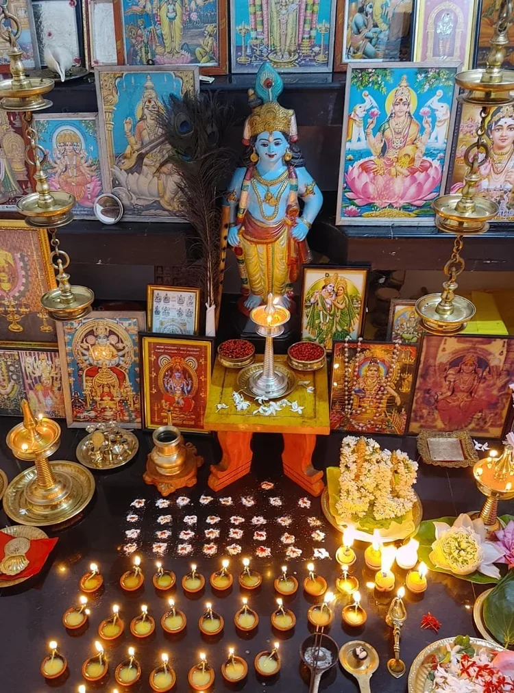 Hindu altar with statues, framed images, oil lamps, flowers, and decorations for worship.