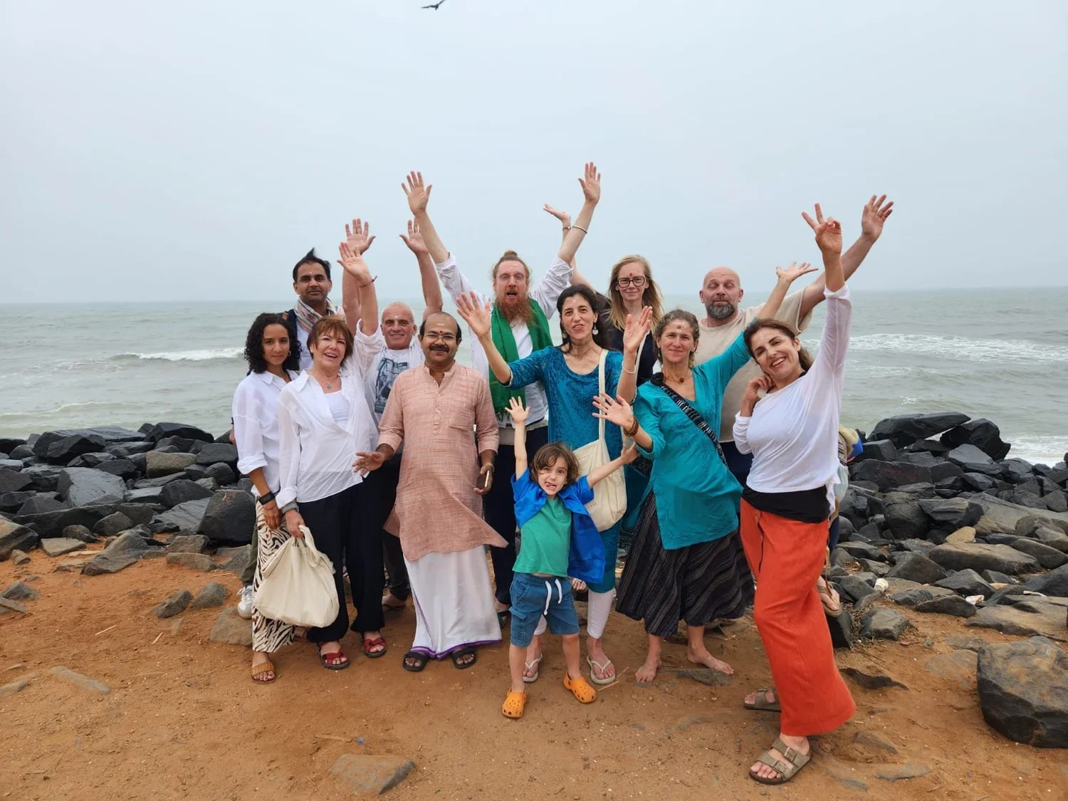 Group of people standing on rocky beach with the ocean in background, smiling and waving.