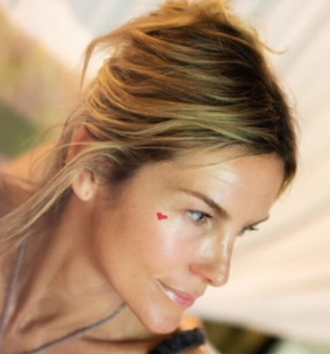 Close-up of a woman with blonde hair and a small heart sticker on her face, looking to the right.